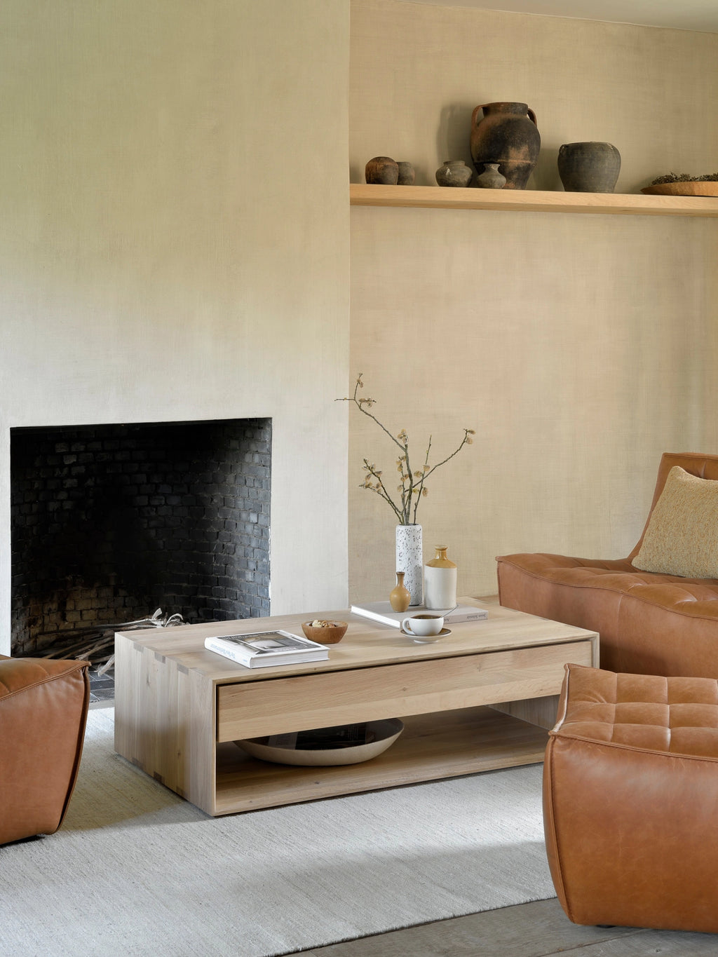 Ethnicraft Nordic Coffee Table, a contemporary 120cm oak coffee table, showcasing its light wood grain and functional open shelf, perfectly complementing a warm, inviting living room setting with leather seating.