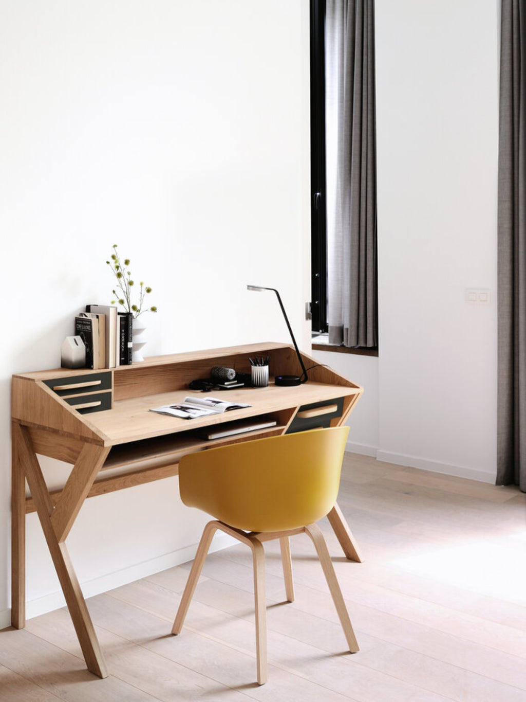 Ethnicraft Origami Desk in black oak, a modern and elegant writing desk with a sloped top, integrated storage, and sleek design, displayed in a bright, minimalist room with a yellow chair.