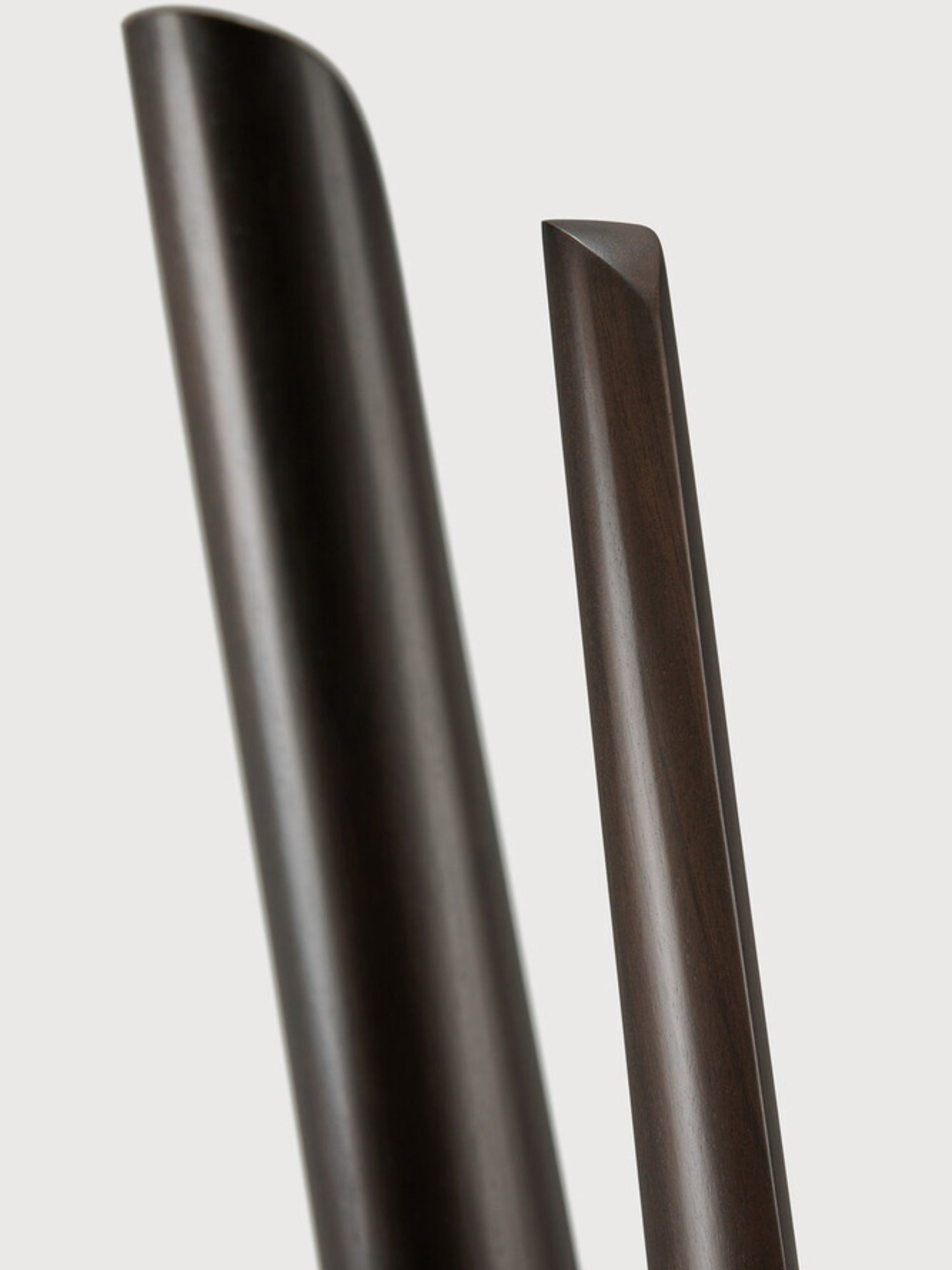 Ethnicraft PI Coat Stand, a modern minimalist coat rack crafted from dark stained solid oak wood, showcasing slender, elegantly curved uprights with a smooth, polished finish and visible wood grain, including a distinctive angled flat top on one element. This organic modern design is ideal for a stylish entryway, contemporary hallway, or sophisticated bedroom accent.