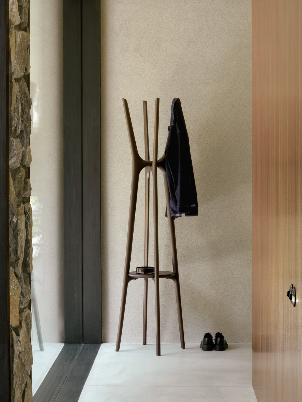Ethnicraft PI Coat Stand, a sculptural organic modern coat rack crafted from solid dark brown wood with a warm, smooth finish. Its branching, minimalist design features multiple hooks and an integrated circular shelf for keys or small items, supported by a stable tripod base. This contemporary wood coat stand is ideal for minimalist entryways, Scandinavian hallways, or as a stylish accent in modern bedrooms and home offices.
