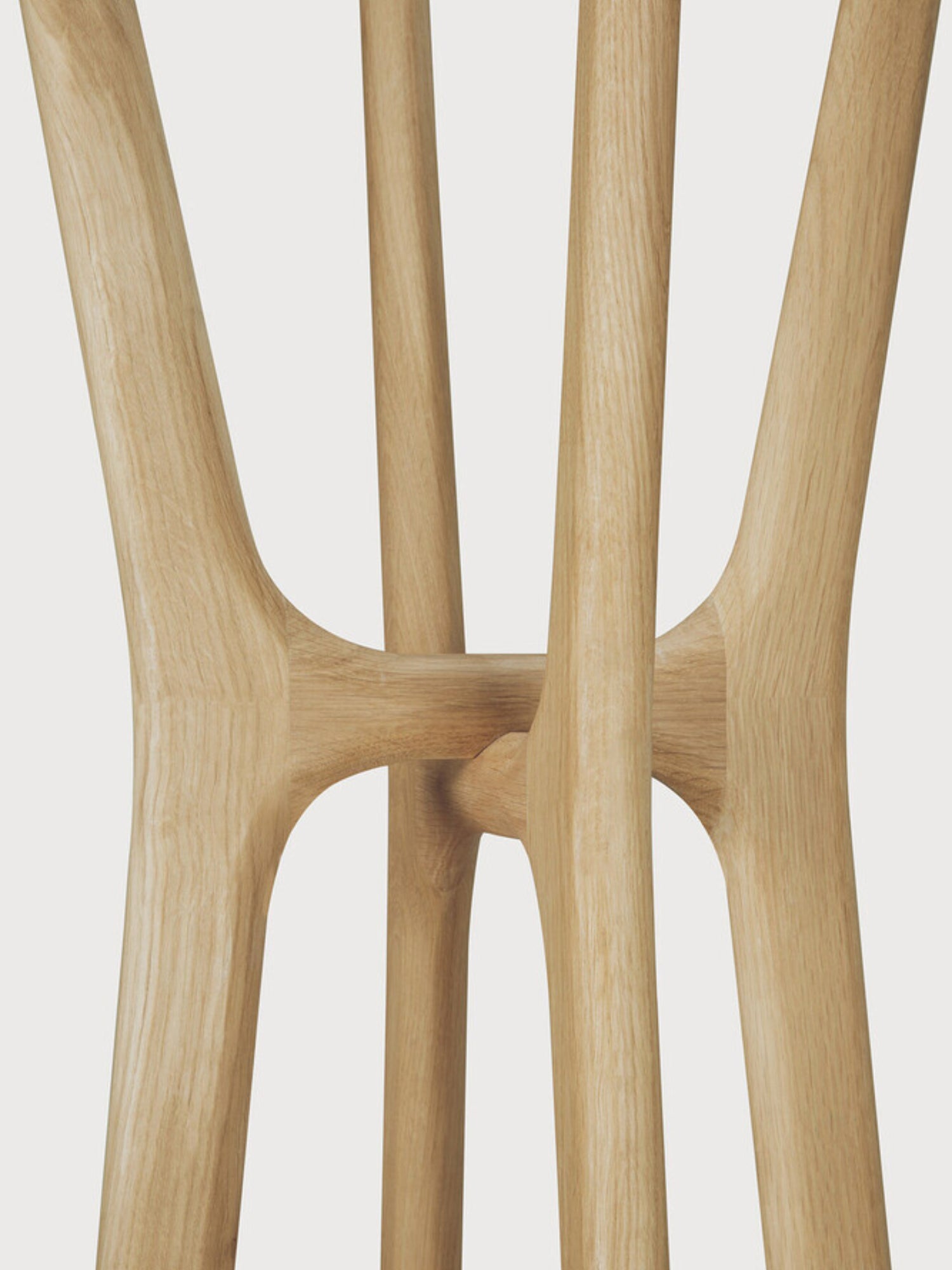 Ethnicraft PI Coat Stand, a sculptural organic modern coat rack crafted from solid natural oak wood, showcasing a light finish and beautiful wood grain. Its unique design features smoothly curved, branching wooden legs that elegantly merge to create a minimalist yet striking form. Ideal as a contemporary entryway coat stand or a stylish hall tree for Scandinavian and modern interiors.