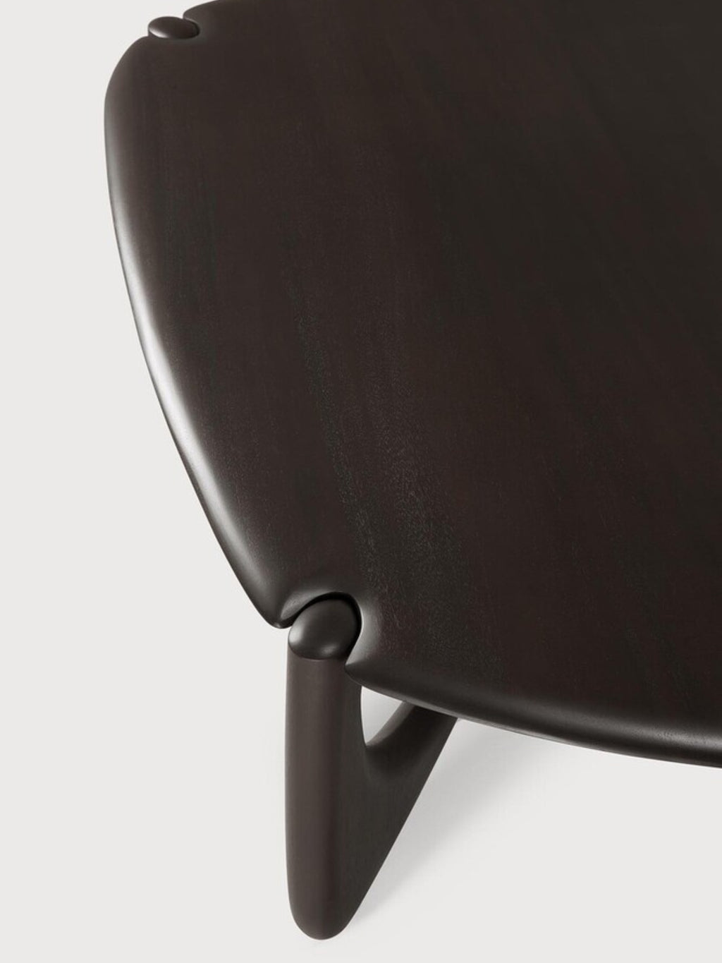 Ethnicraft PI Coffee Table in Mahogany Dark Brown, Pebble shape. Detailed view of the table's corner, showcasing the smooth, dark brown mahogany wood, the rounded edges, and the elegant, curved leg design, displayed on a white background.