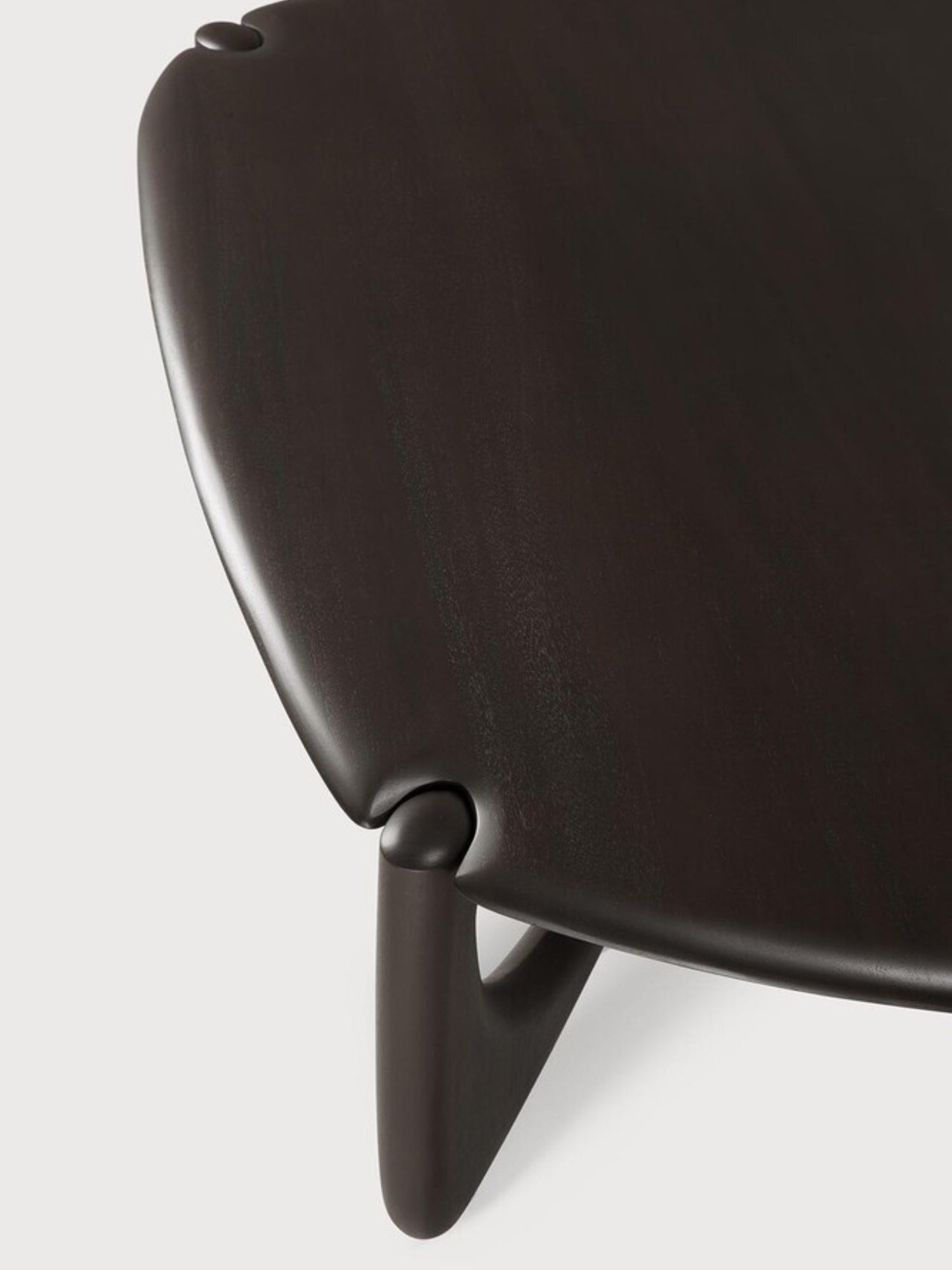 Ethnicraft PI Coffee Table in Mahogany Dark Brown, Pebble shape. Detailed view of the table's corner, showcasing the smooth, dark brown mahogany wood, the rounded edges, and the elegant, curved leg design, displayed on a white background.