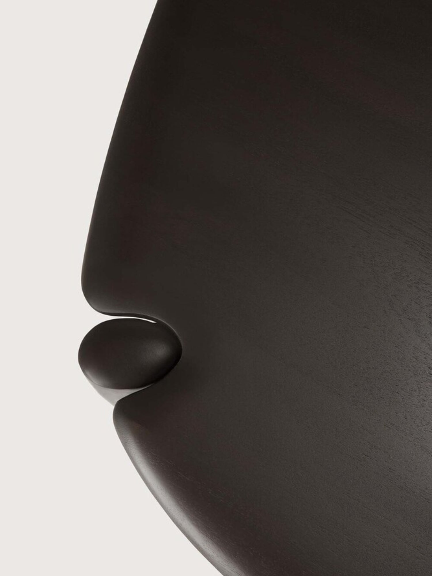 Ethnicraft PI Coffee Table in Mahogany Dark Brown, Pebble shape. Overhead close-up detail of the dark brown mahogany tabletop, focusing on the seamless, organic connection where the leg meets the table, emphasizing the smooth, natural wood grain.
