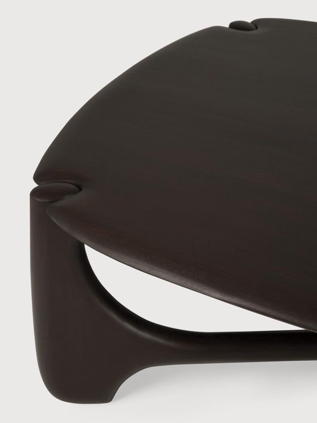 Ethnicraft PI Coffee Table in Mahogany Dark Brown, Pebble shape. Angled close-up of the table's edge, highlighting the smooth, dark brown mahogany wood and the unique, rounded, pebble-like shape of the tabletop and leg connection.