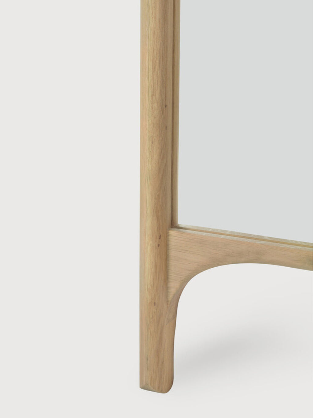 Ethnicraft PI Floor Mirror, a modern full-length mirror featuring a robust frame crafted from natural solid oak wood with visible grain. Its clean lines are softened by a distinctive curved, organic detail at the base, giving it a contemporary and minimalist aesthetic. This Scandinavian-inspired oak standing mirror is perfect for a modern bedroom, elegant entryway, or dressing area.