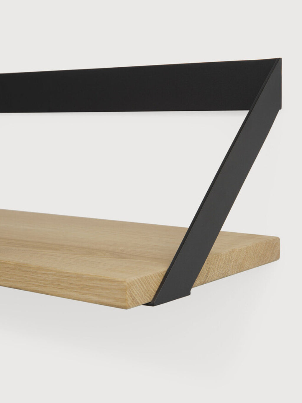 Ethnicraft Ribbon Shelf, a modern minimalist wall shelf featuring a thick solid oak wood plank with visible grain, supported by a striking matte black metal geometric bracket. This contemporary floating shelf offers stylish display and storage for Scandinavian, industrial chic, or modern interiors in living rooms or home offices.