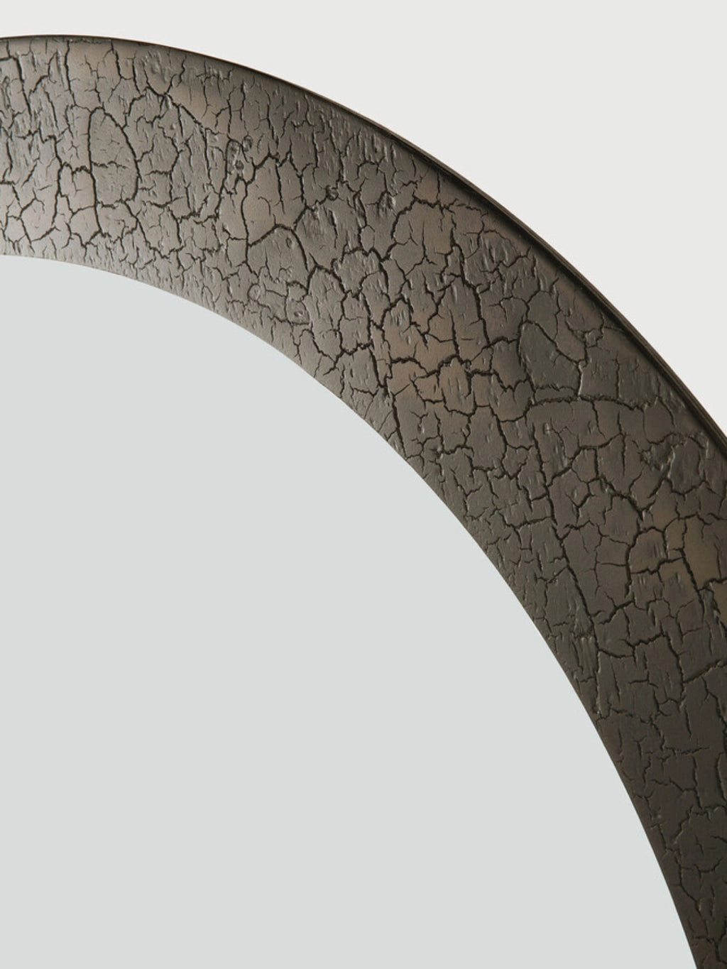 Ethnicraft Sphere Wall Mirror, a round wall mirror featuring a unique dark grey textured metal frame with a distinctive cracked, distressed finish. This organic modern mirror showcases a rugged, almost volcanic-like surface in deep charcoal tones, providing an industrial chic aesthetic. Perfect as a decorative mirror for an entryway, living room, or bedroom, adding a touch of rustic elegance to contemporary interiors.