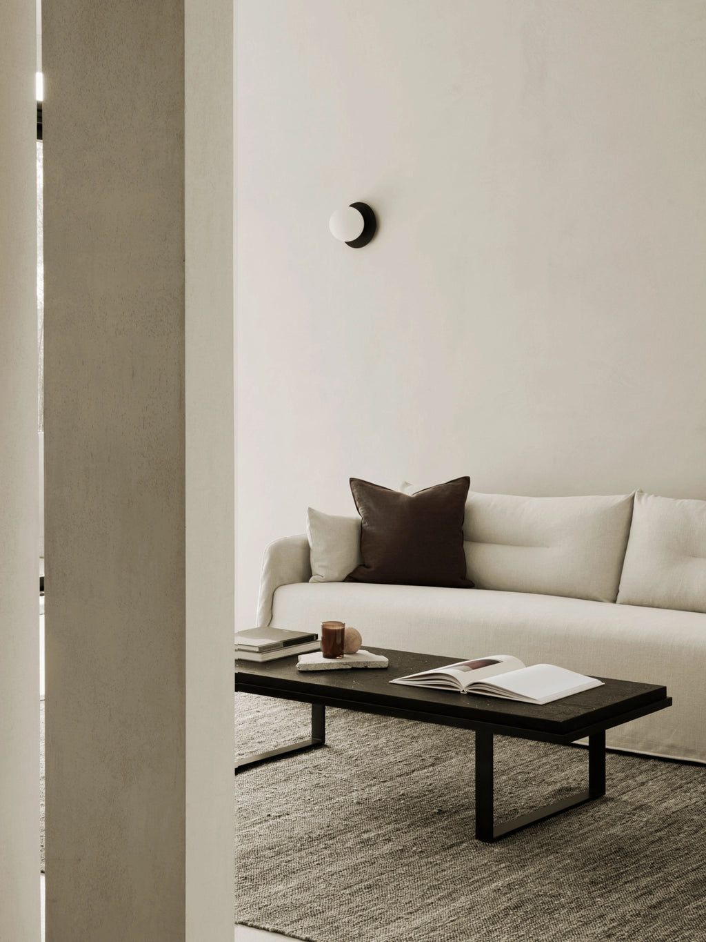 Ethnicraft Stability Coffee Table in umber, a stylish rectangular coffee table with a dark, textured top and sleek metal base, positioned in a modern living room setting with a light-colored sofa and rug.