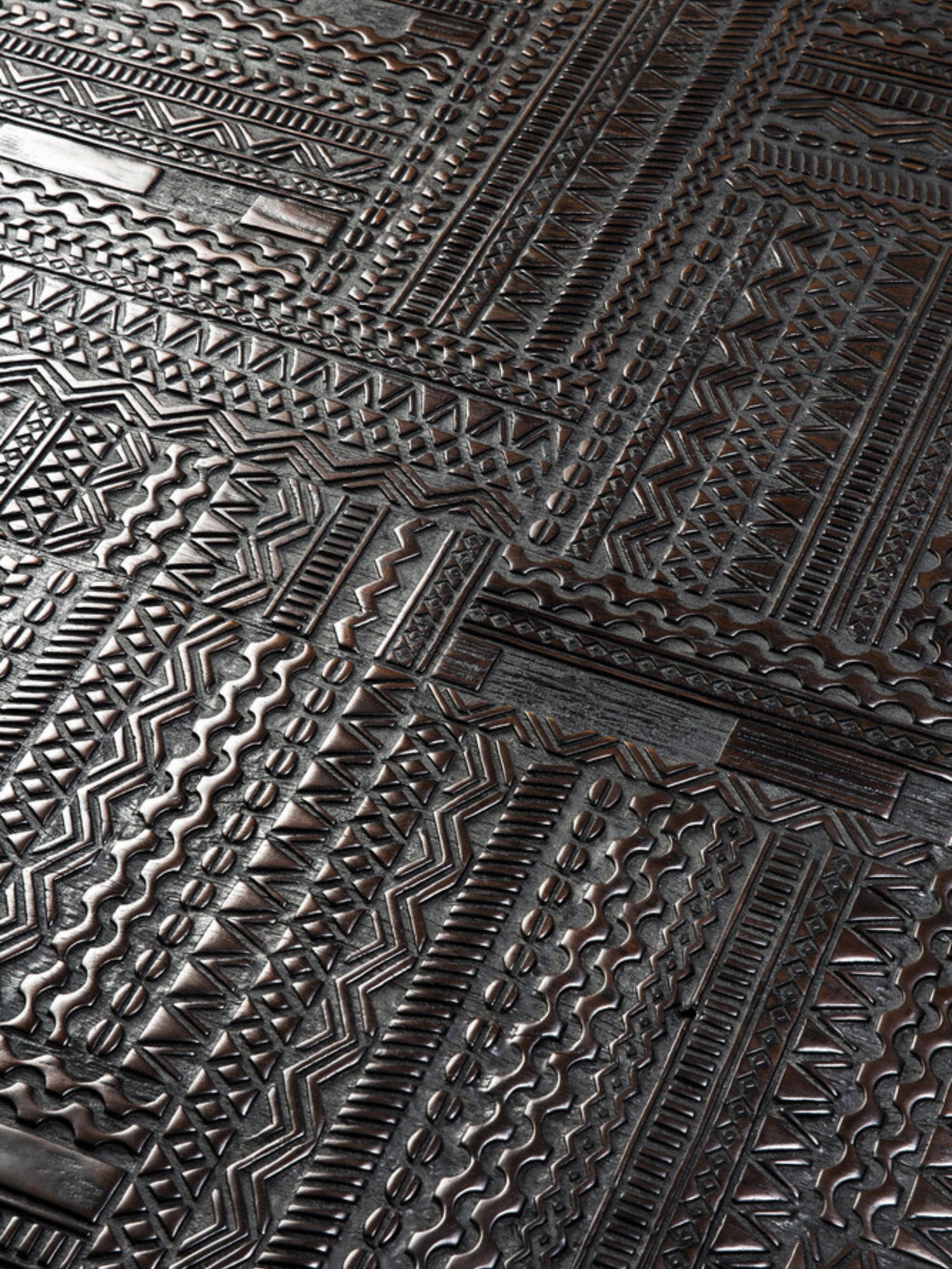 Ethnicraft Tabwa Coffee Table, a close-up detail shot revealing the rich, dark wood and the deeply carved, geometric patterns that define this premium and artistic furniture piece, highlighting its unique texture.