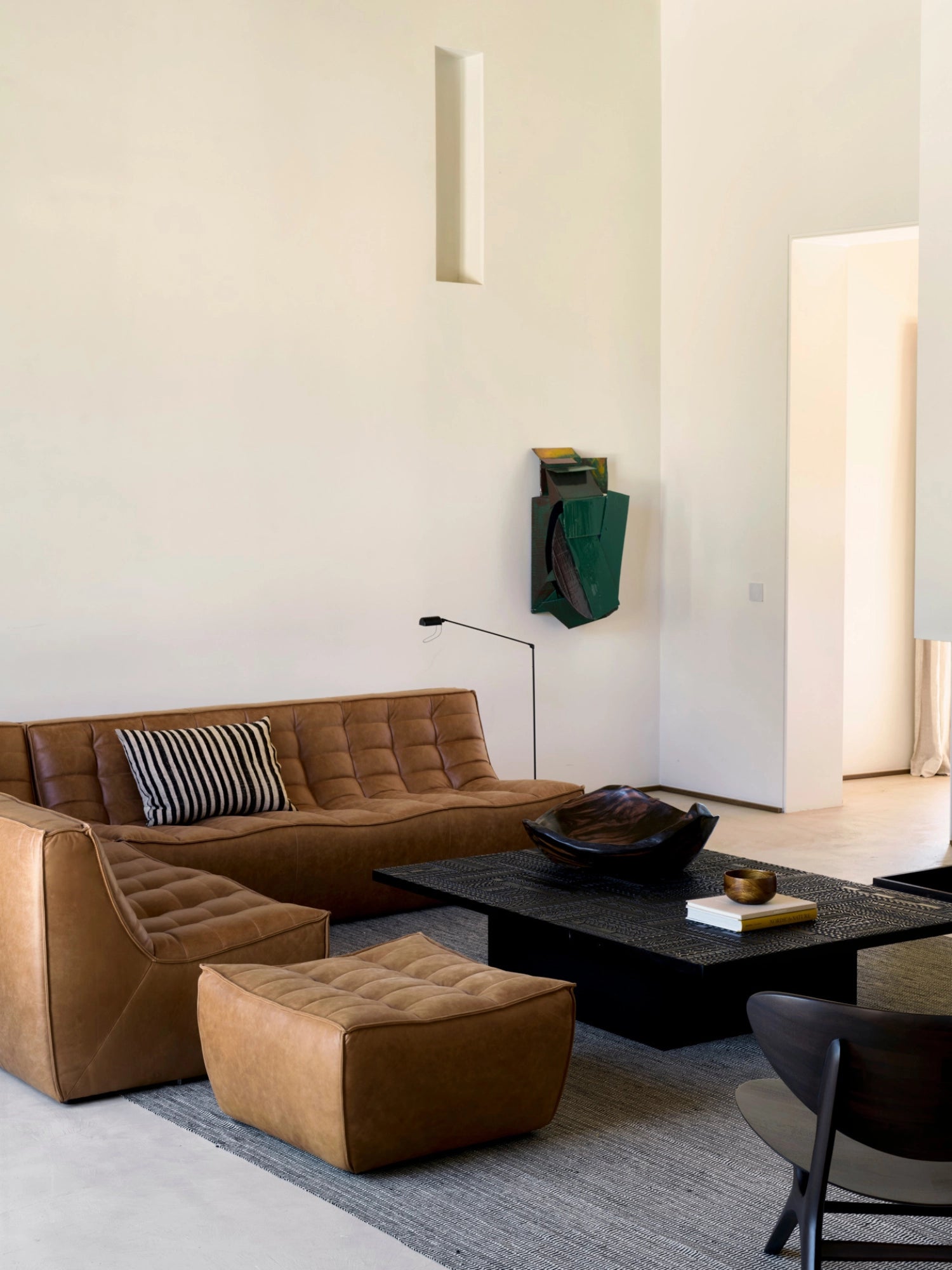 Ethnicraft Tabwa Coffee Table, a bold rectangular black table featuring detailed geometric carvings, positioned in front of a luxurious tan leather sofa, creating a sophisticated and inviting living space.