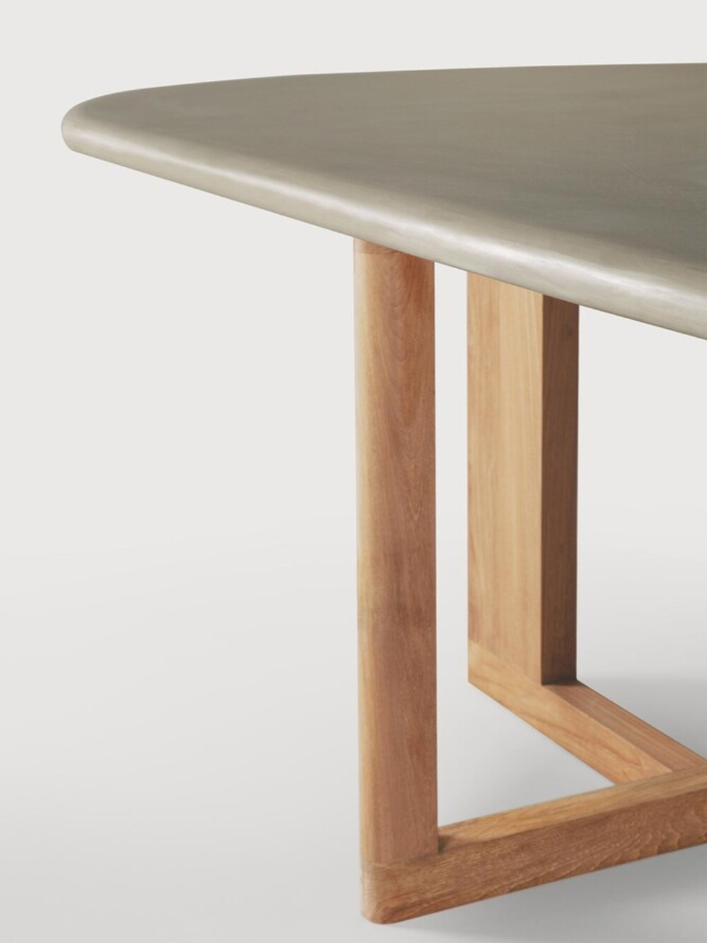 Ethnicraft Trestle Outdoor Dining Table, featuring a smooth, matte greige mineral composite top with an organic, softly rounded pebble shape.