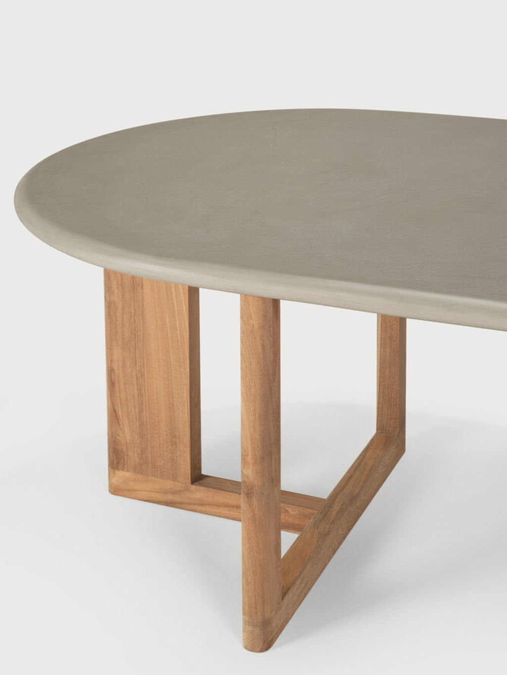 Ethnicraft Trestle Outdoor Dining Table, featuring a smooth, oval light grey concrete tabletop paired with a sturdy, architectural trestle base crafted from natural warm brown teak wood. This modern and minimalist dining table is perfect for contemporary outdoor living spaces, patios, or garden areas, offering durable and stylish al fresco dining.