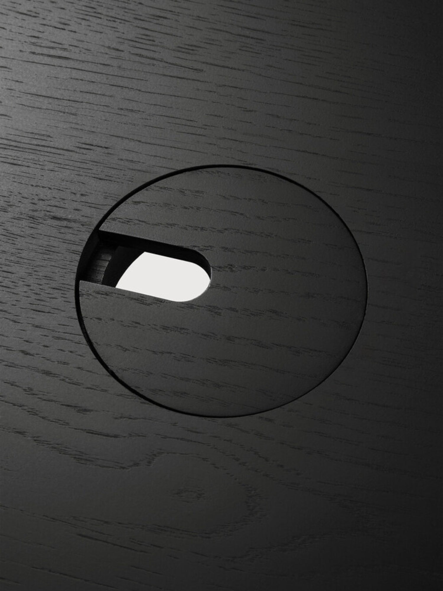 Ethnicraft U Desk, a contemporary black oak desk, featuring a detailed view of the integrated circular cable management grommet with a subtle opening, highlighting its functional design.