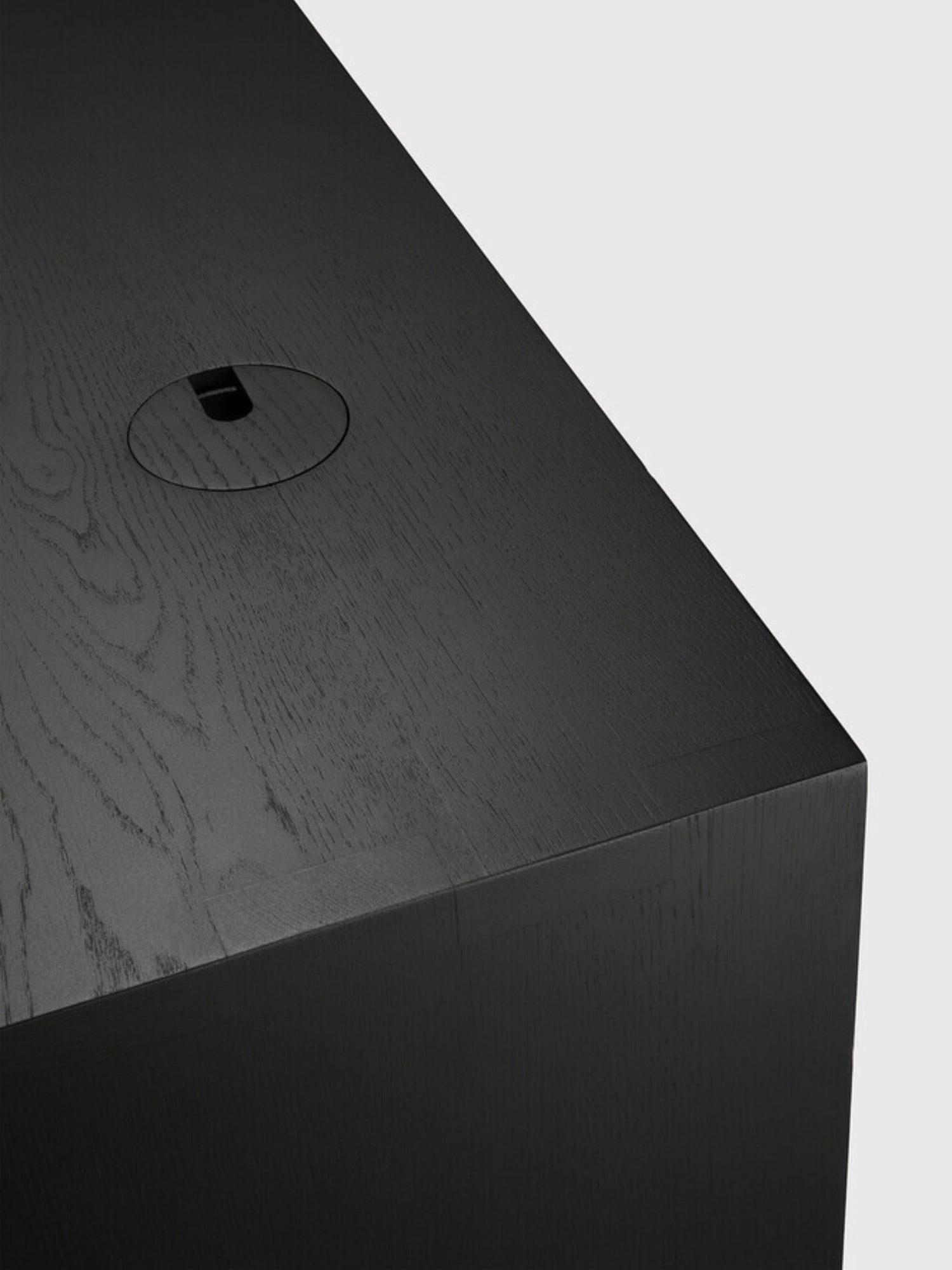 Ethnicraft U Desk in black oak, a detailed shot of the dark wood surface with a visible grain and an integrated circular cable management grommet, combining style and function.