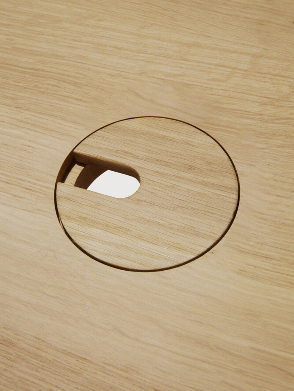 Ethnicraft U Desk, a close-up of the circular cable management grommet on the natural oak wood surface, designed for seamless wire organization and a tidy workspace.