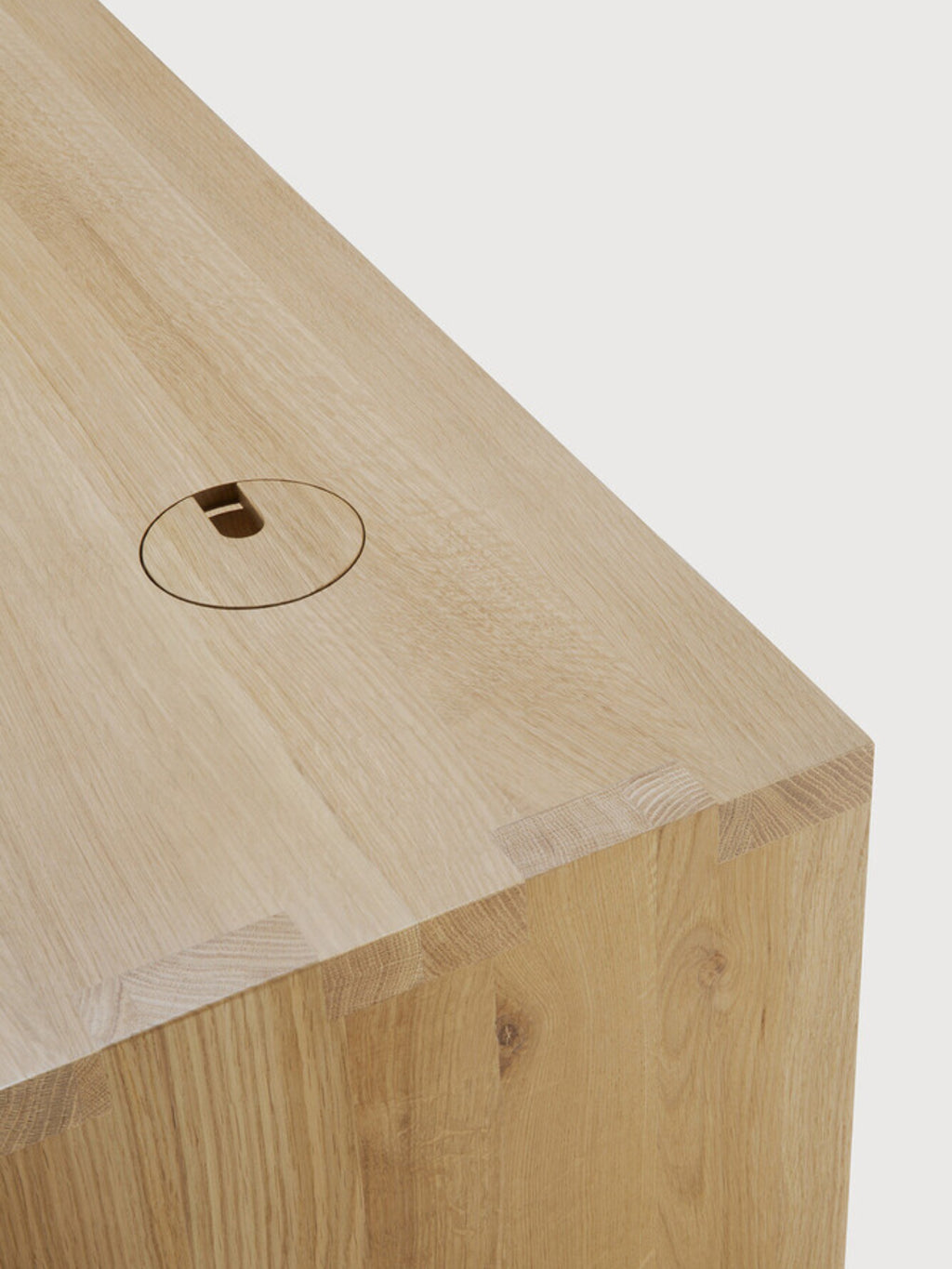 Ethnicraft U Desk, a detailed view of the natural oak wood surface, highlighting the subtle grain and a cleverly integrated circular cable management grommet on the tabletop.