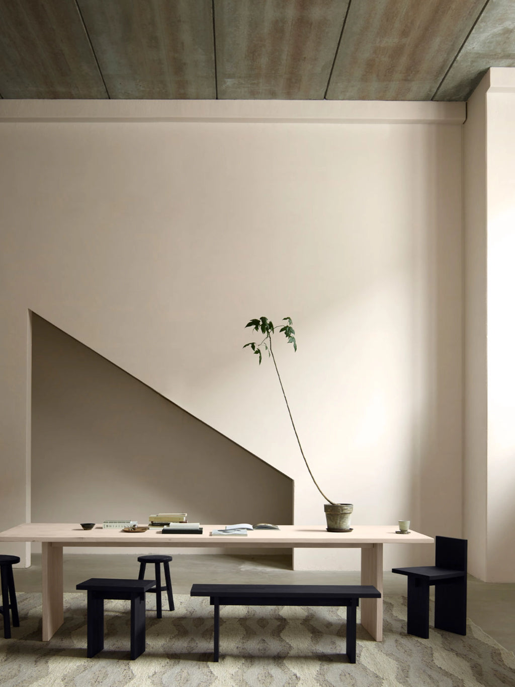 Tine K Koru Bench, a striking matte black solid wood bench with a thick, sculptural rectangular top and robust, block-like legs, embodying a modern minimalist aesthetic with a brutalist edge. Ideal as a bold dining bench for contemporary dining rooms, a minimalist entryway console, or an accent piece in Scandinavian-inspired spaces.