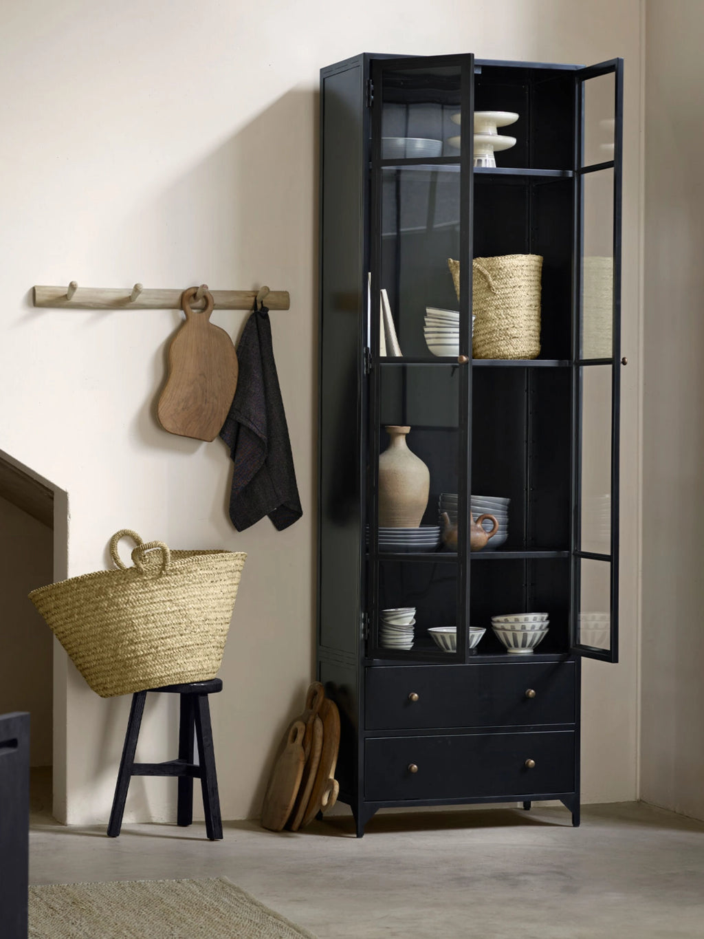 Tine K Metal High Cabinet, a tall industrial chic display cabinet crafted from matte black metal with two glass-paned doors revealing multiple interior shelves, and two solid lower drawers accented with antique brass knob handles. This modern minimalist storage cabinet is perfect for organizing and showcasing items in a living room, dining room, or home office.