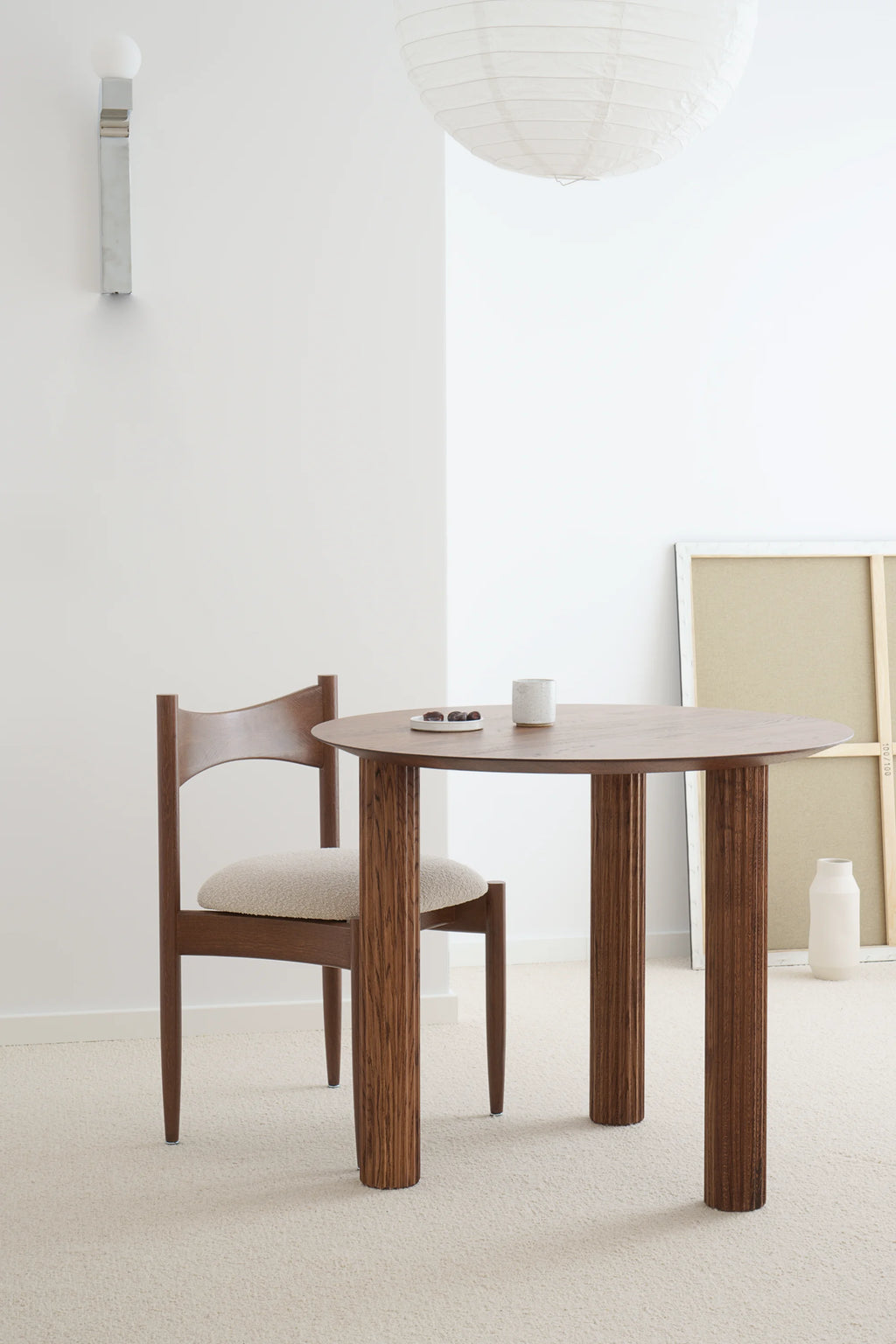 TAMO Filar Round Dining Table, showcasing a premium dark brown wood finish with distinctive fluted legs. Styled with a mid-century modern chair and a clean white cup. Perfect for creating a stylish, intimate dining space.