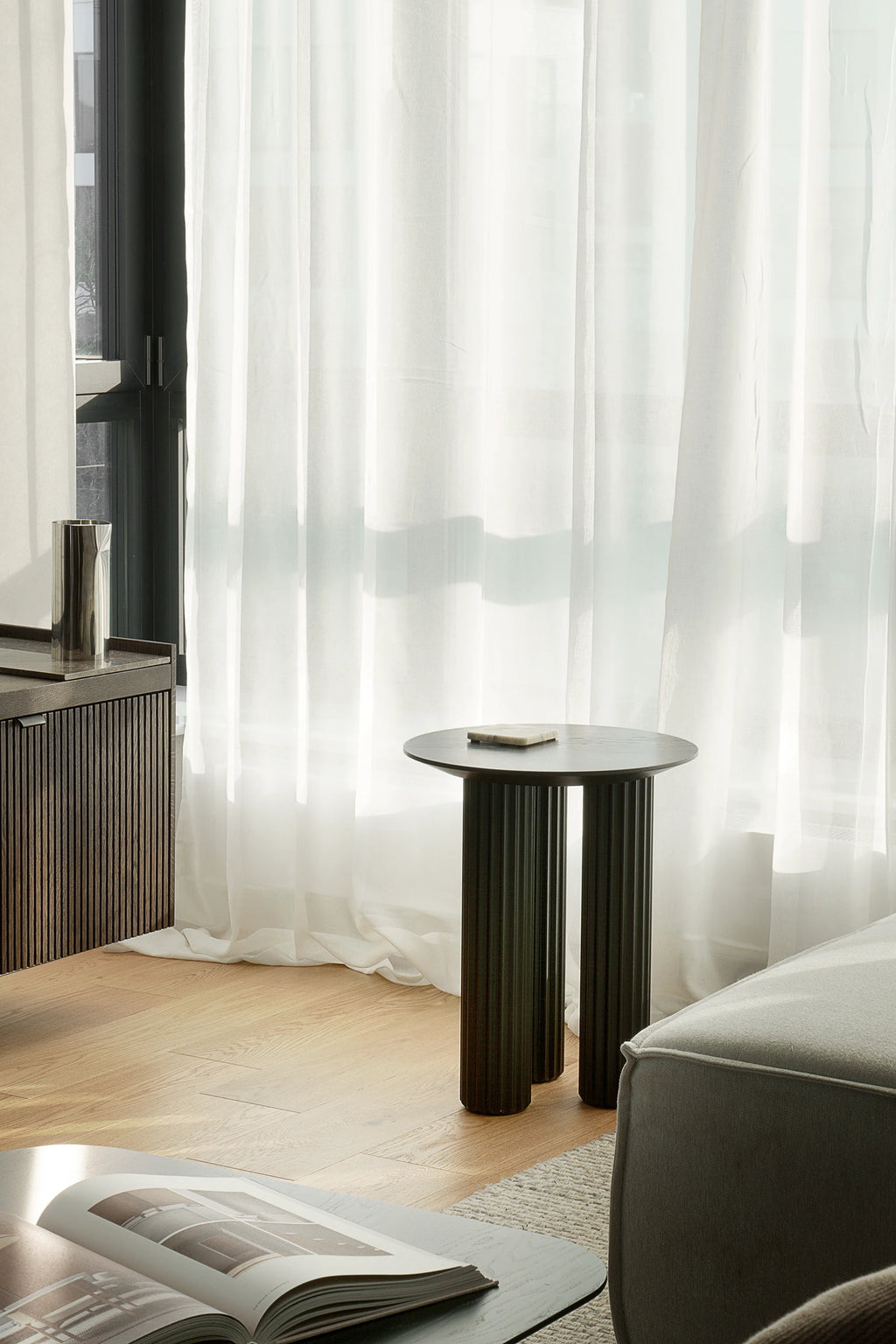 TAMO Filar Side Table in a lifestyle shot, featuring a dark brown, round top and three fluted cylindrical legs. A premium, modern accent piece for any living space.