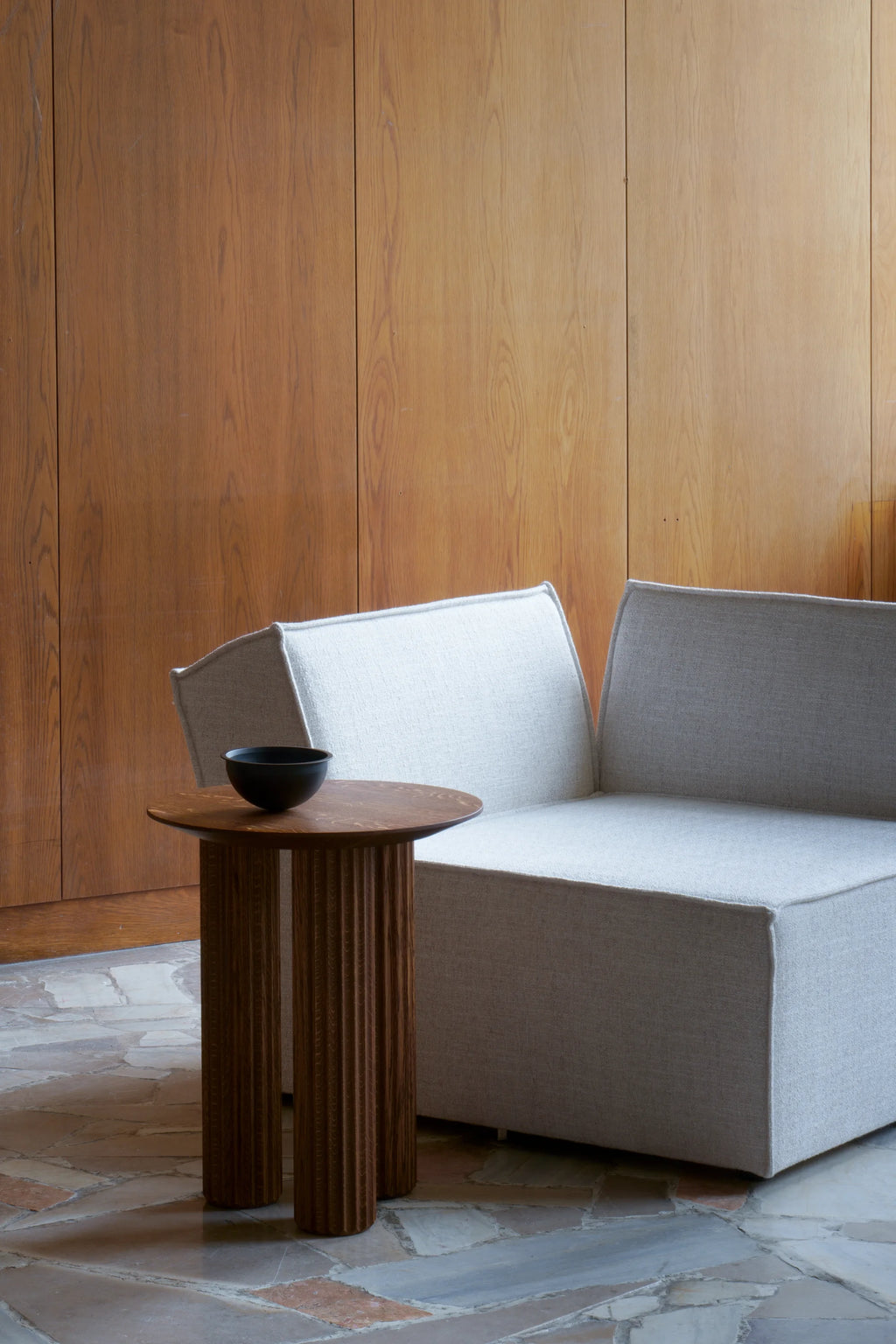 TAMO Filar Side Table, a premium dark brown fluted oak wood table with a round top, styled next to a light grey sofa. Ideal for modern living spaces.
