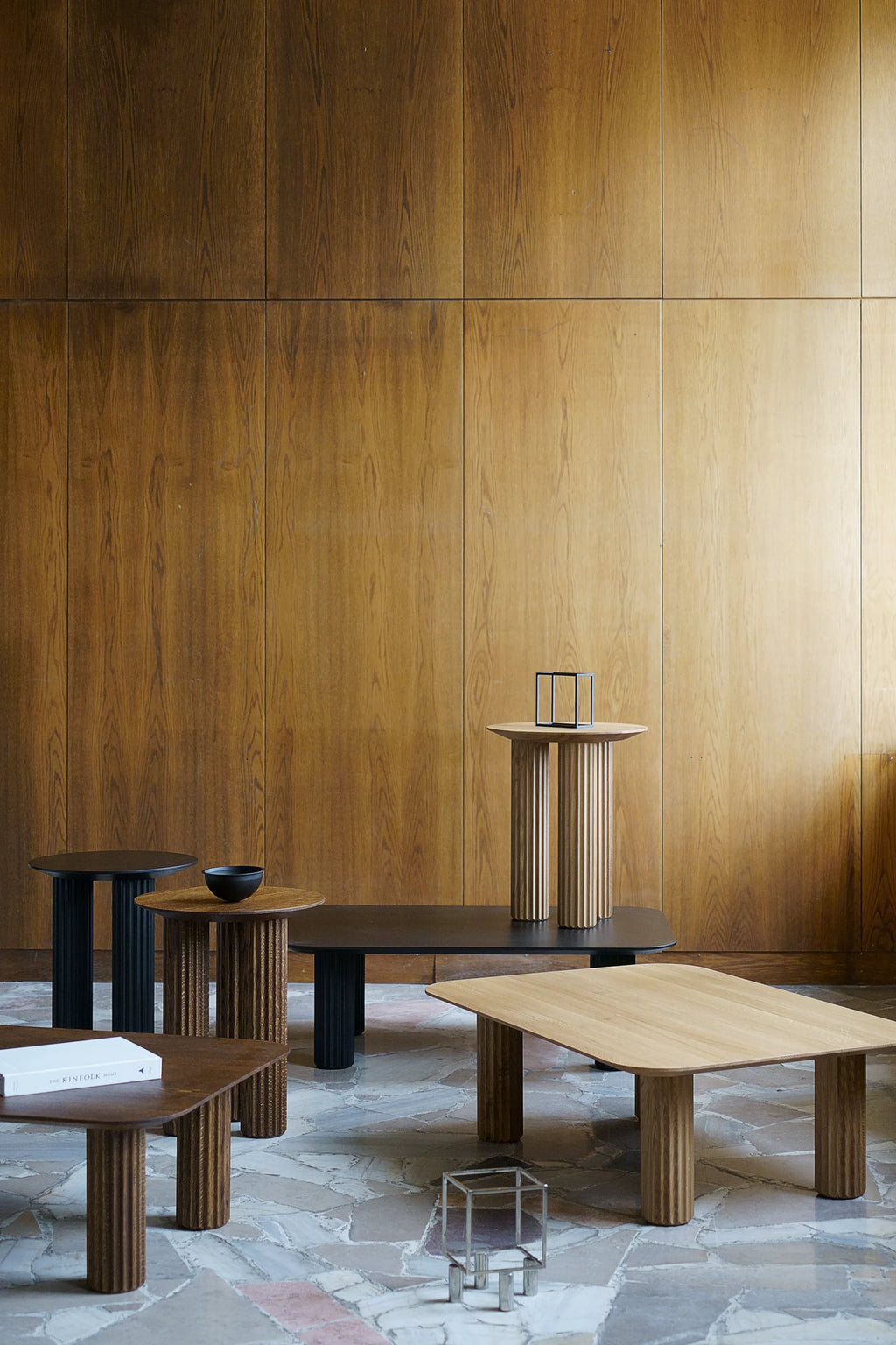 TAMO Filar Side Table collection, featuring round and rectangular tables in light and dark oak wood, some with black tops, showcasing unique ridged column legs in a modern showroom setting. These luxury side tables offer versatile styling.