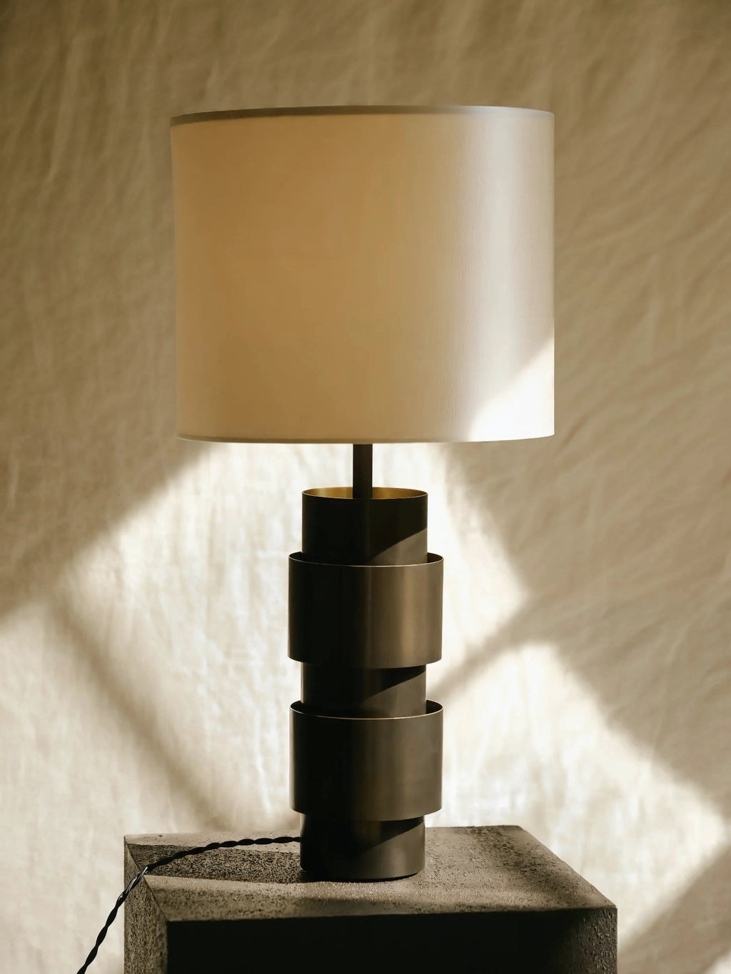 CTO Lighting Ring Table Lamp in a sophisticated bronze finish, highlighting its unique stacked cylindrical base and a soft cream fabric shade, with dappled sunlight.