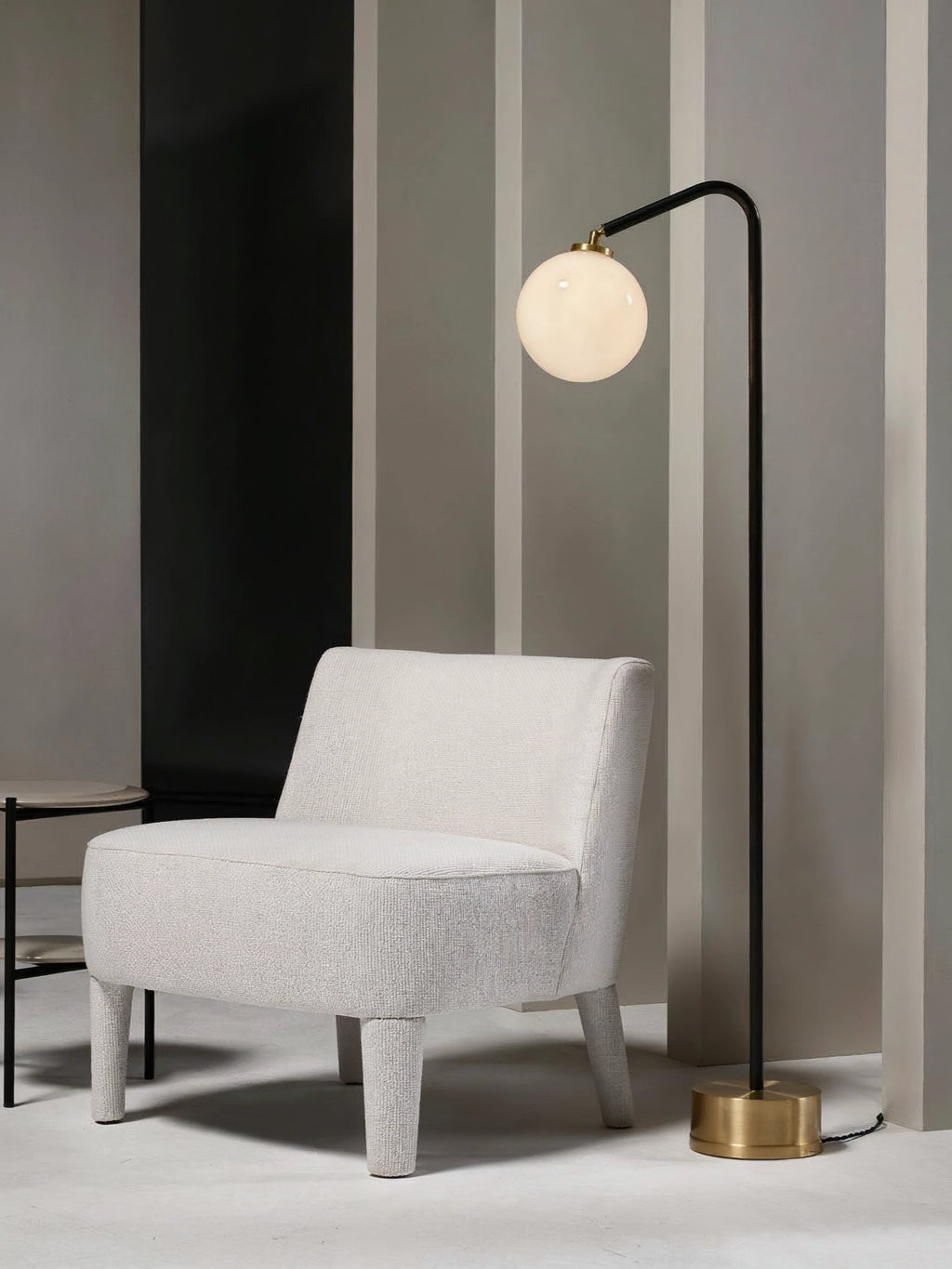 CTO Lighting Oscar Floor Lamp, featuring a sleek black metal frame and a glowing opal glass sphere, positioned next to a textured white armchair in a contemporary room.