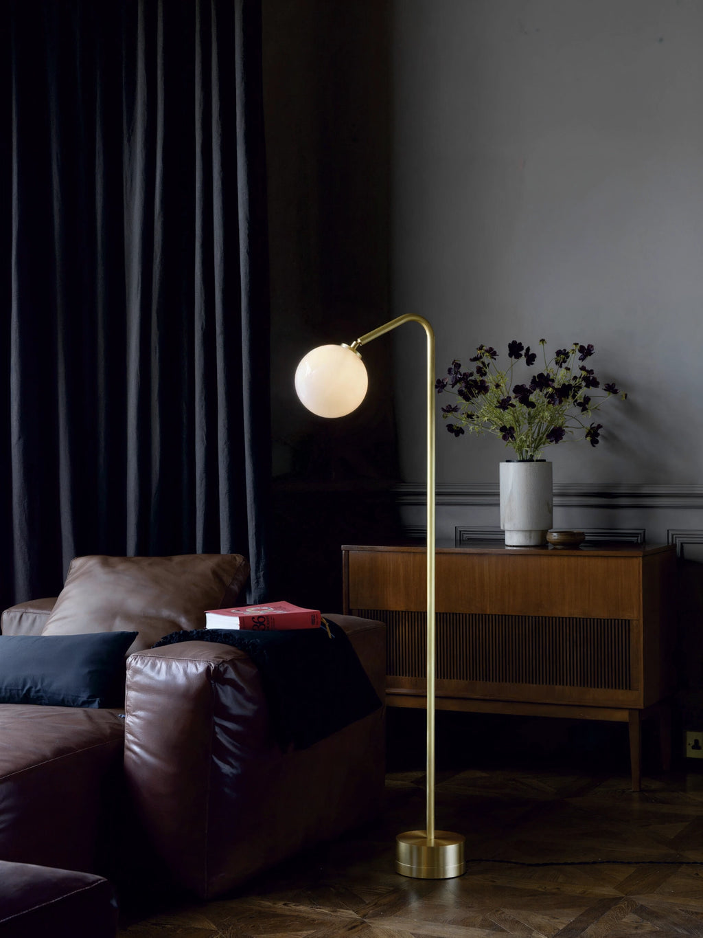 CTO Lighting Oscar Floor Lamp, showcasing its elegant brass finish and white spherical shade, casting a warm glow in a cozy living room with a brown leather sofa.
