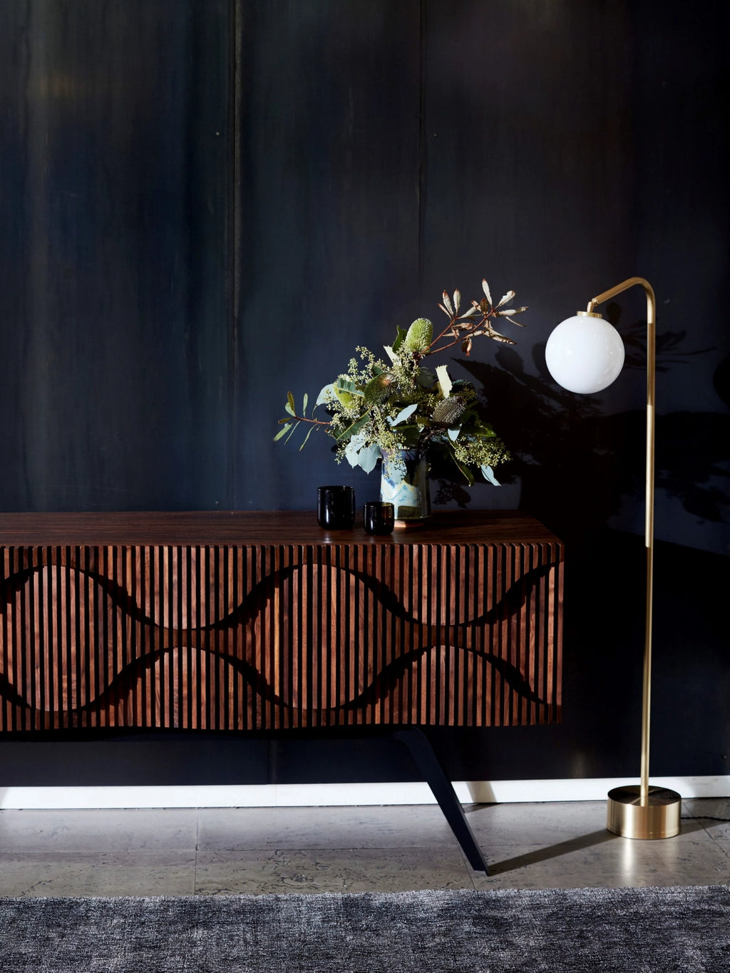 CTO Lighting Oscar Floor Lamp, a modern brass floor lamp with a spherical opal glass diffuser, illuminating a dark, sophisticated living space with a wooden console.