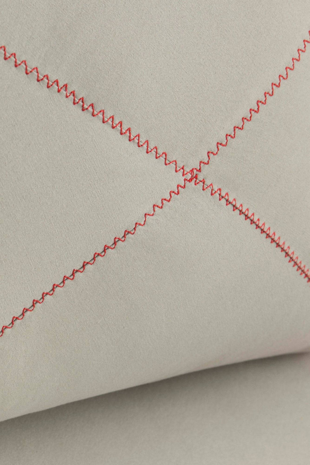 GAN Rugs Grapy Lounge Chair, showcasing a close-up of its soft light greige fabric upholstery detailed with a striking diagonal quilted pattern of bright red zigzag stitching.