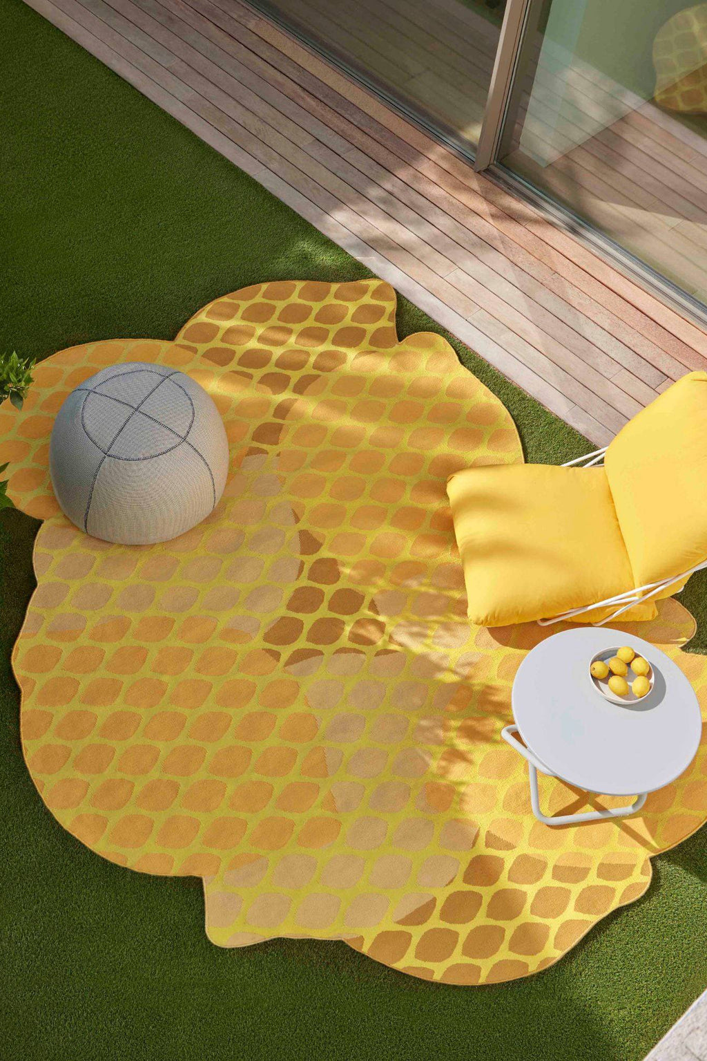 GAN Rugs Citrus Outdoor Rug, a vibrant yellow and orange area rug designed with an irregular, organic lemon slice shape and a playful, repeating leaf-like pattern. This modern outdoor rug features a durable flat weave, showcasing varying shades of yellow, lime green, and golden orange, perfect for adding a pop of color. Ideal for creating a cheerful and contemporary outdoor living space, patio, balcony, or garden decor.