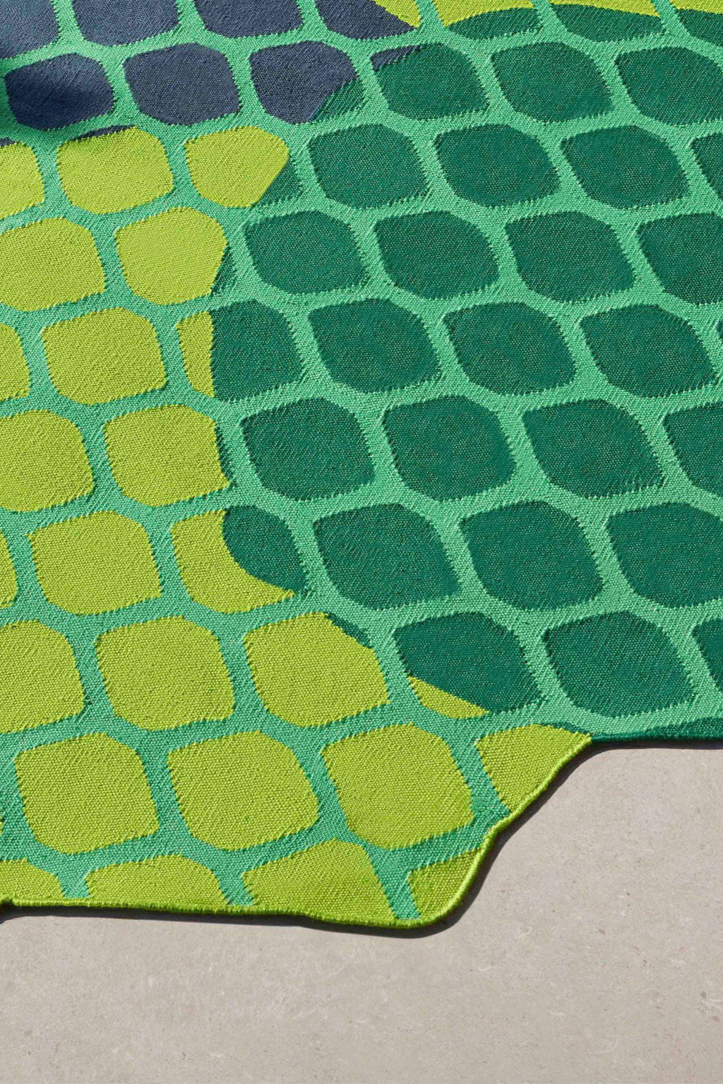 GAN Rugs Citrus Outdoor Rug, a vibrant modern outdoor area rug featuring an irregular organic shape and a bold abstract pattern of rounded pebble-like motifs. It showcases a lively color palette of bright lime green, emerald green, and dark teal, with subtle hints of navy blue, all crafted from durable woven material with a textured flatweave finish. Perfect for adding a playful, contemporary touch to patios, decks, or any outdoor living space.