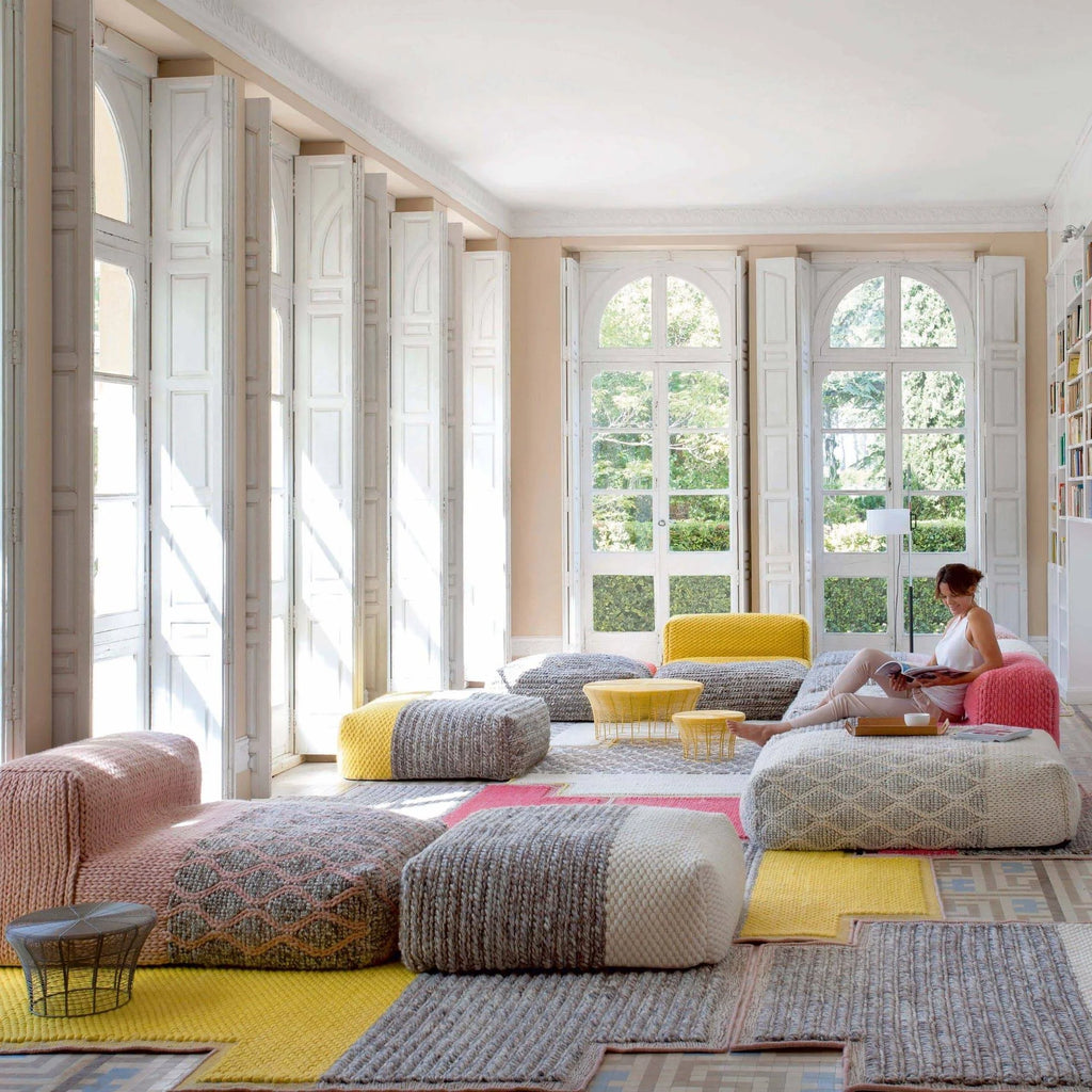 GAN Rugs Mangas Space Plait Lounge, a vibrant modular sofa system crafted from chunky hand-knitted wool in a palette of blush pink, bright yellow, soft grey, and cream.