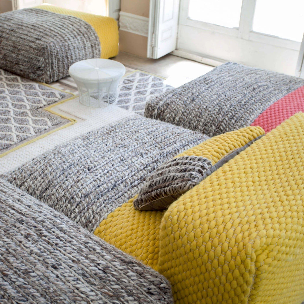 GAN Rugs Mangas Space Plait Lounge, a modern modular sofa featuring chunky hand-knitted and hand-woven wool sections in warm grey, vibrant yellow, and coral pink.