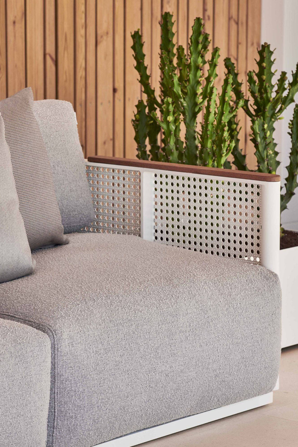 Gandia Blasco Bosc 3-Seater Sofa, a modern outdoor sofa featuring light grey textured fabric upholstery with plush cushions, set on a sleek white aluminum frame. Its distinctive design includes white perforated metal side panels and warm dark wood armrest details, offering a contemporary take on outdoor lounge seating. This stylish 3-seater patio sofa is perfect for minimalist garden designs, poolside lounging, or a sophisticated terrace.