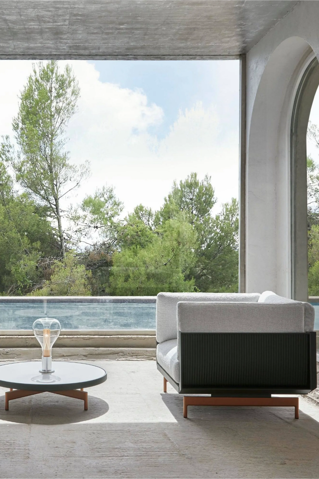Gandia Blasco Onde Lounge Chair, a modern outdoor lounge chair featuring plush light grey upholstered cushions and a distinctive dark grey ribbed aluminum panel on the side. This contemporary patio furniture piece sits on sleek terracotta-colored metal legs, offering a minimalist yet comfortable design. Ideal for luxury outdoor living rooms, modern patios, or sophisticated garden spaces.