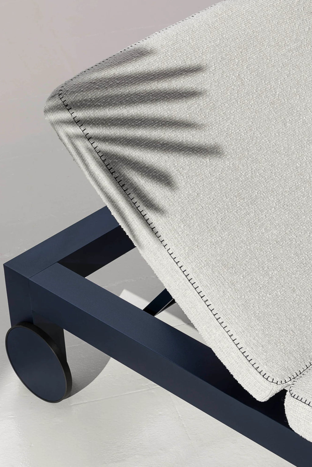 Gandia Blasco Islablanca Outdoor Chaise Lounge, a modern minimalist sunbed featuring a deep matte navy blue aluminum frame with clean rectangular lines and integrated dark wheels for easy movement. It is topped with a thick, light grey textured outdoor fabric cushion, detailed with prominent dark decorative stitching along the edges. Ideal for luxury poolside lounging or contemporary patio and deck spaces.