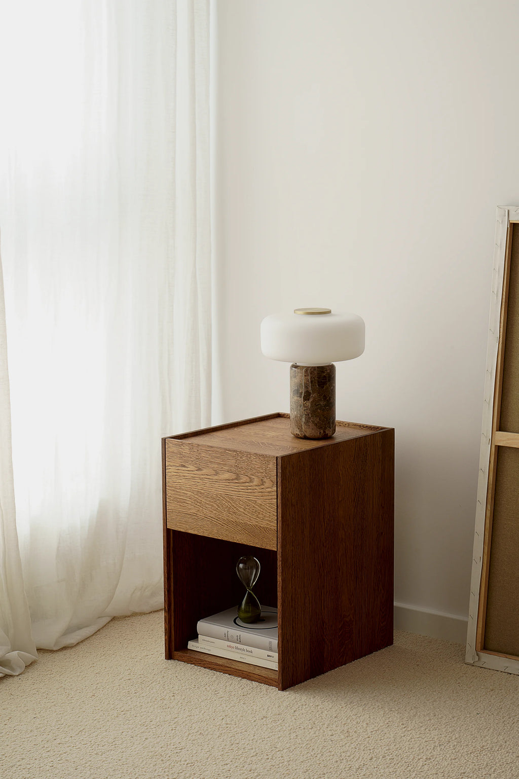 TAMO Kari Nightstand, a premium dark brown wood nightstand with a light oak drawer and open shelf, displayed in a minimalist room with a lamp and books. Ideal for modern bedroom decor.