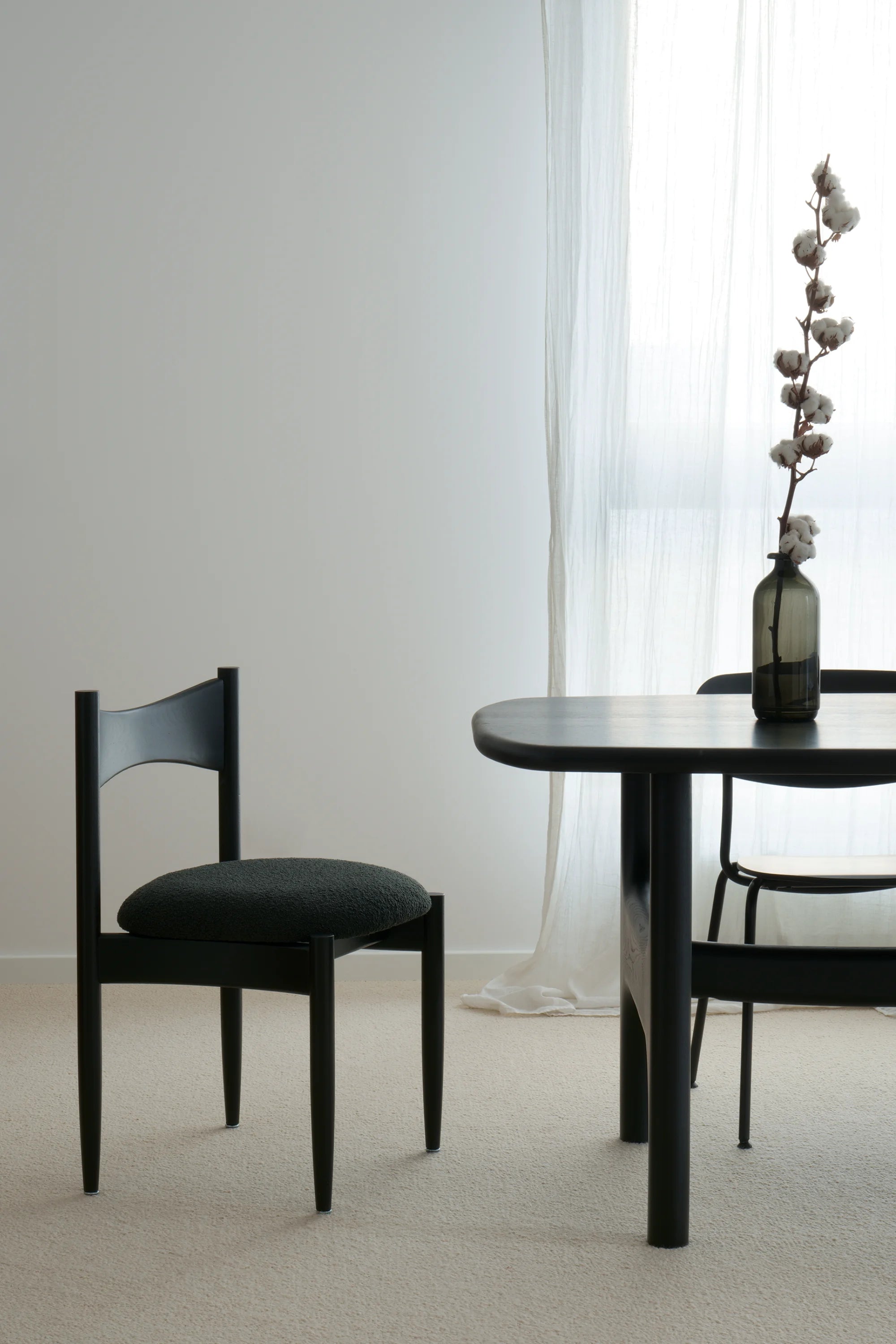 Black dining table and chairs in a minimalistic room with white walls and curtains.