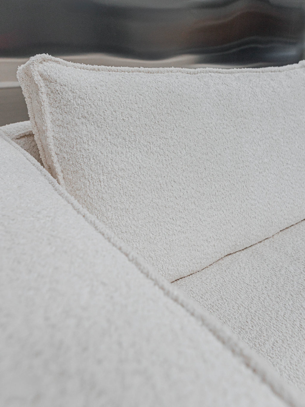 Tinted Objects Klinge Sofa, a close-up of the luxurious, textured off-white bouclé fabric upholstery on a modern sofa backrest and seat cushion. This elegant, comfortable sofa is ideal for creating a cozy, stylish living space for discerning homeowners.