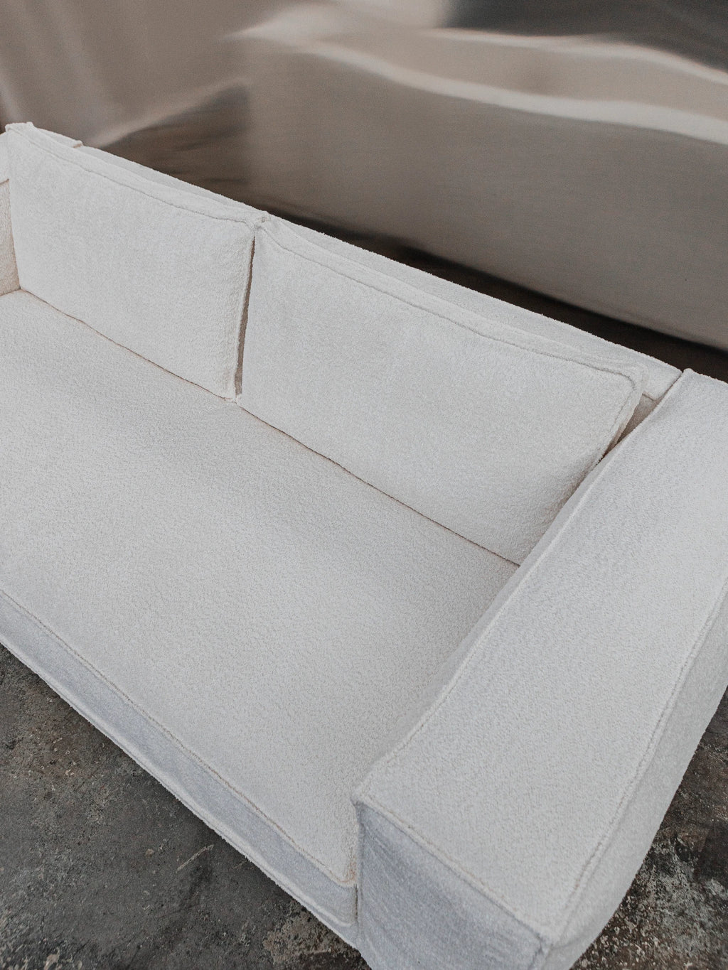 Tinted Objects Klinge Sofa, a modern off-white bouclé sofa with plush, textured fabric and clean lines. This stylish and comfortable couch is perfect for contemporary living rooms seeking elegant seating.