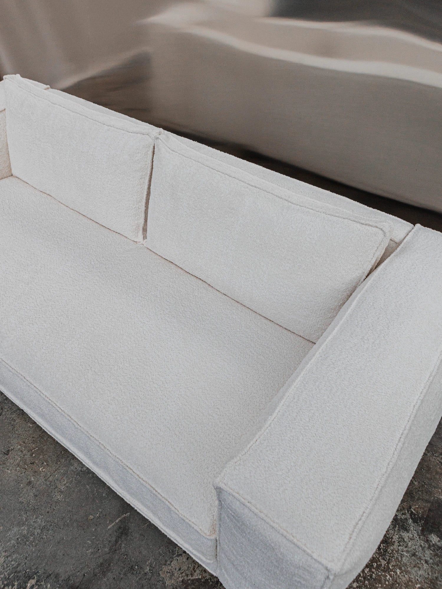 Tinted Objects Klinge Sofa, a modern off-white bouclé sofa with plush, textured fabric and clean lines. This stylish and comfortable couch is perfect for contemporary living rooms seeking elegant seating.