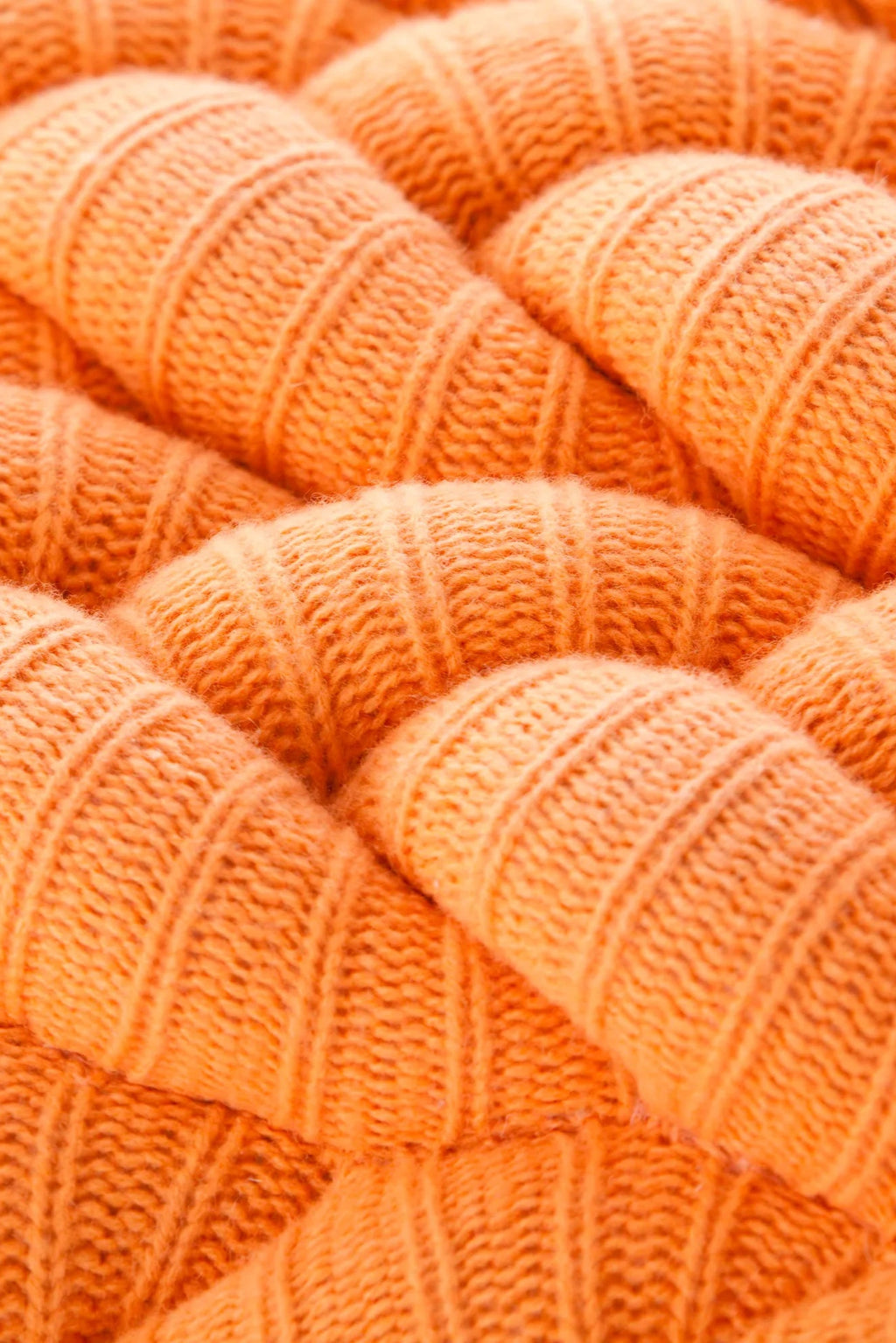 GAN Rugs Knitted Stool, a vibrant tangerine orange knitted pouf with a plush, soft ribbed texture, crafted from a chunky wool blend yarn. This cozy and modern accent stool offers a comfortable, organic shape, perfect for adding a pop of color and warmth to contemporary living rooms, minimalist bedrooms, or stylish children's rooms.