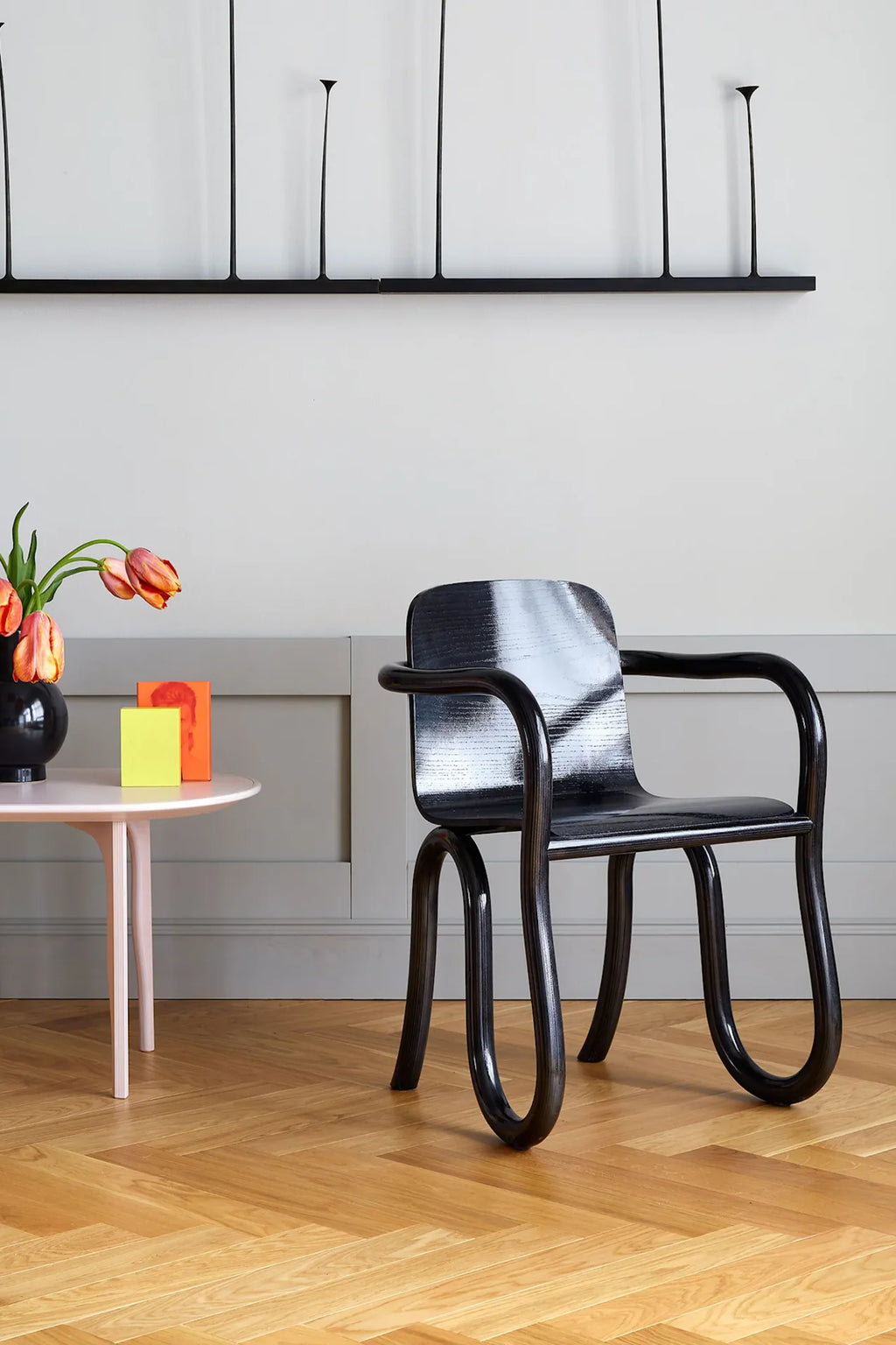 Made by Choice Kolho Dining Chair in a sophisticated black finish, featuring a modern, minimalist design with unique curved wooden legs and armrests, placed in a stylish room setting with wooden floors.