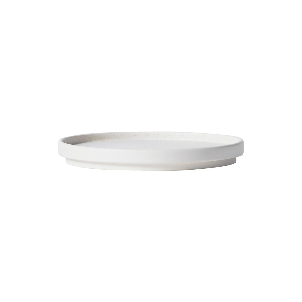 Kristina Dam Setomono Plate S - Set of 4, a modern minimalist stoneware plate in a clean off-white color with subtle dark speckles and a matte, subtly textured finish. It features a flat, round surface with a gently raised rim and a distinct, elevated base, embodying Scandinavian design principles. Perfect as contemporary tableware for elegant dining or as a versatile serving dish for a minimalist kitchen.