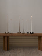 Set of handcrafted and hand-dipped long-lasting and dripless taper candles in assorted colors on a wooden designer bench.
