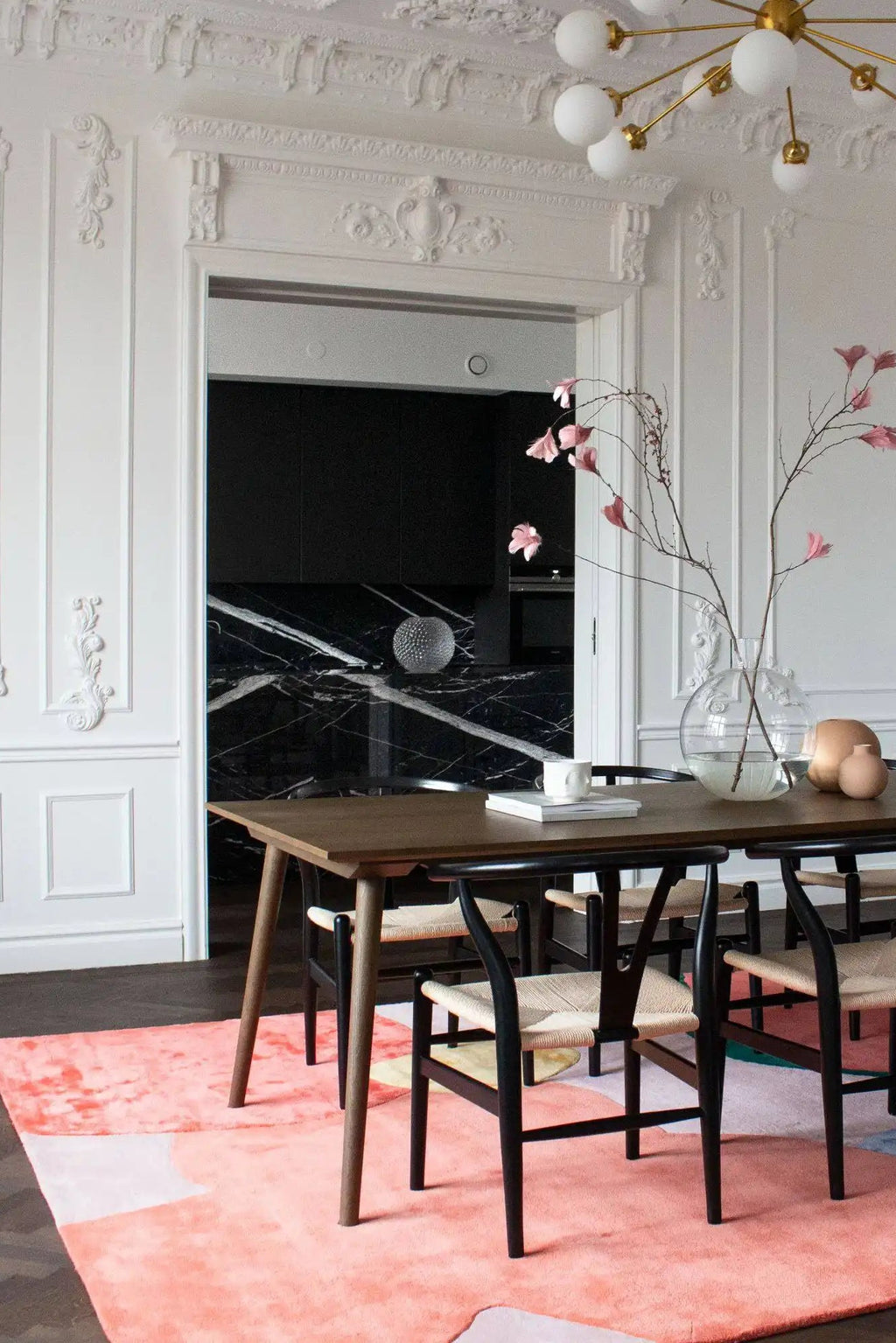 Layered Flower Field Wool Rug, a vibrant abstract area rug in shades of coral, pink, and yellow, placed under a wooden dining table. Perfect for adding a modern, colorful touch to contemporary livi...