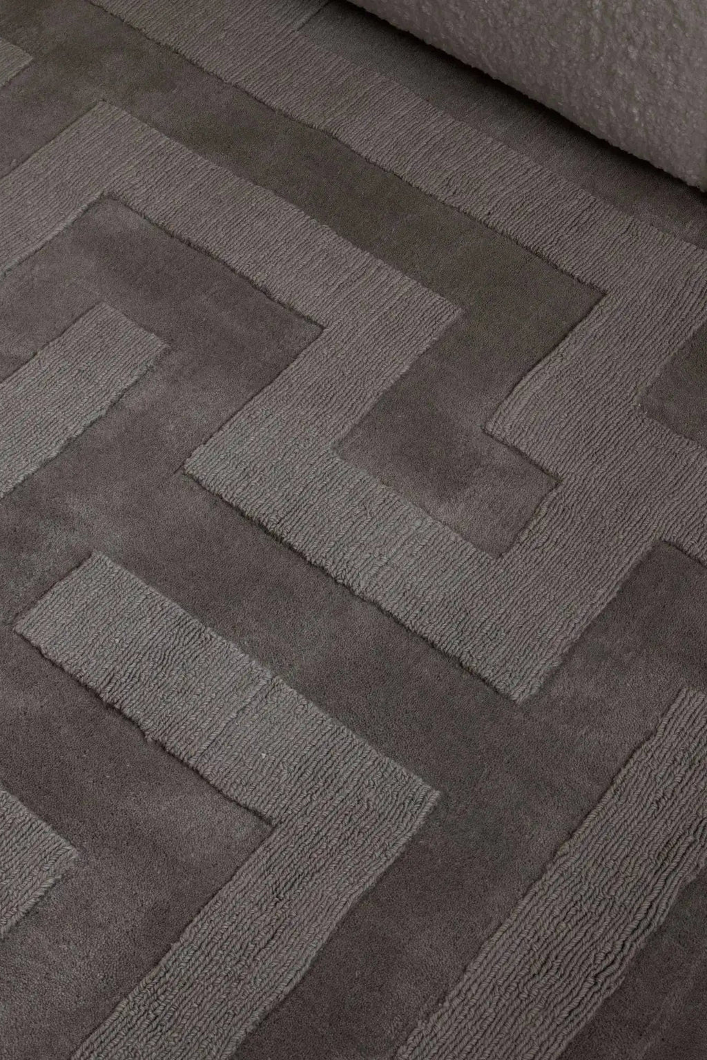 Layered Byzantine Grand Wool Rug, a luxurious dark gray wool rug with a raised geometric maze pattern in varying textures. Perfect for adding a sophisticated and warm touch to modern living spaces.